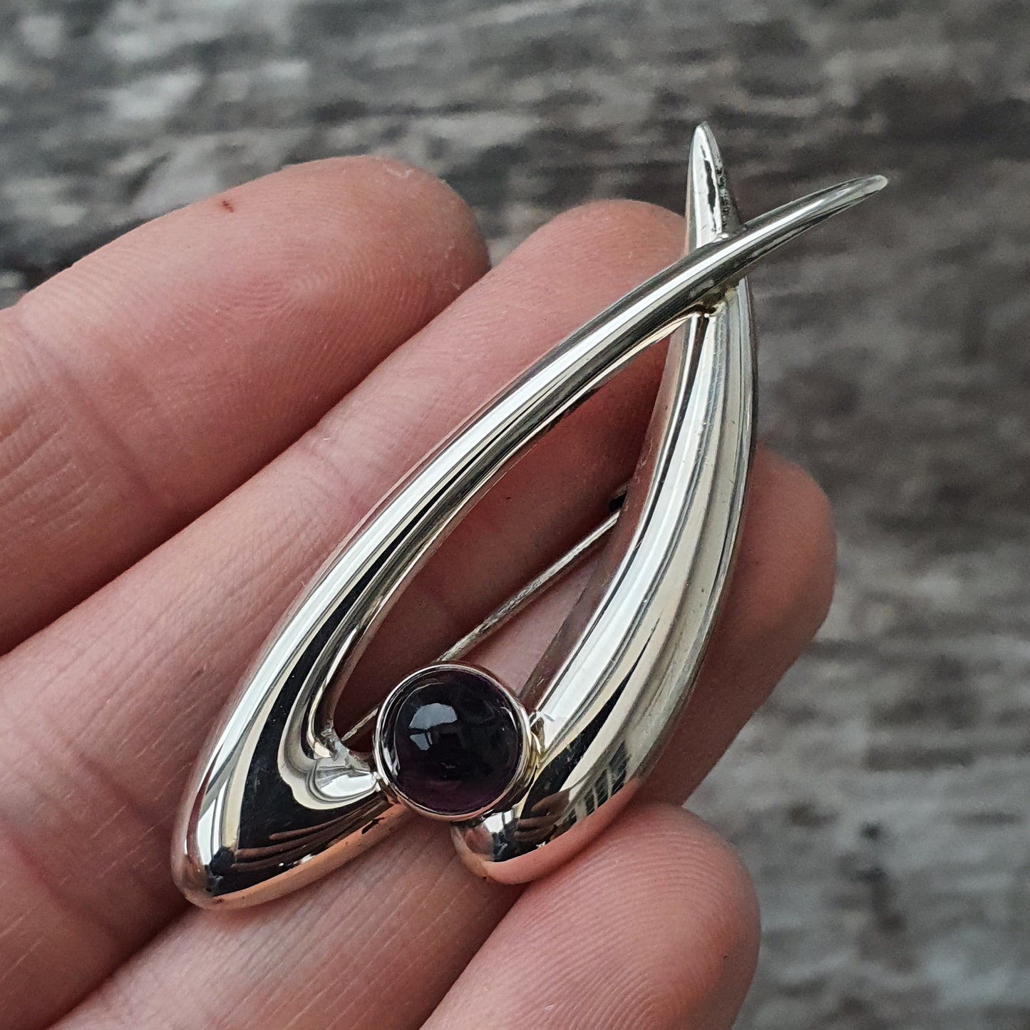 Silver pendant with a teardrop shape and a dark gemstone.