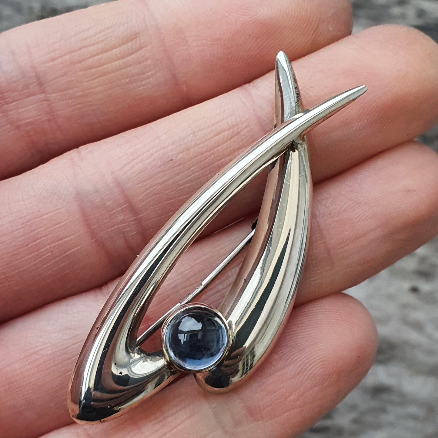 Silver pendant with an abstract curved design and a blue gemstone.