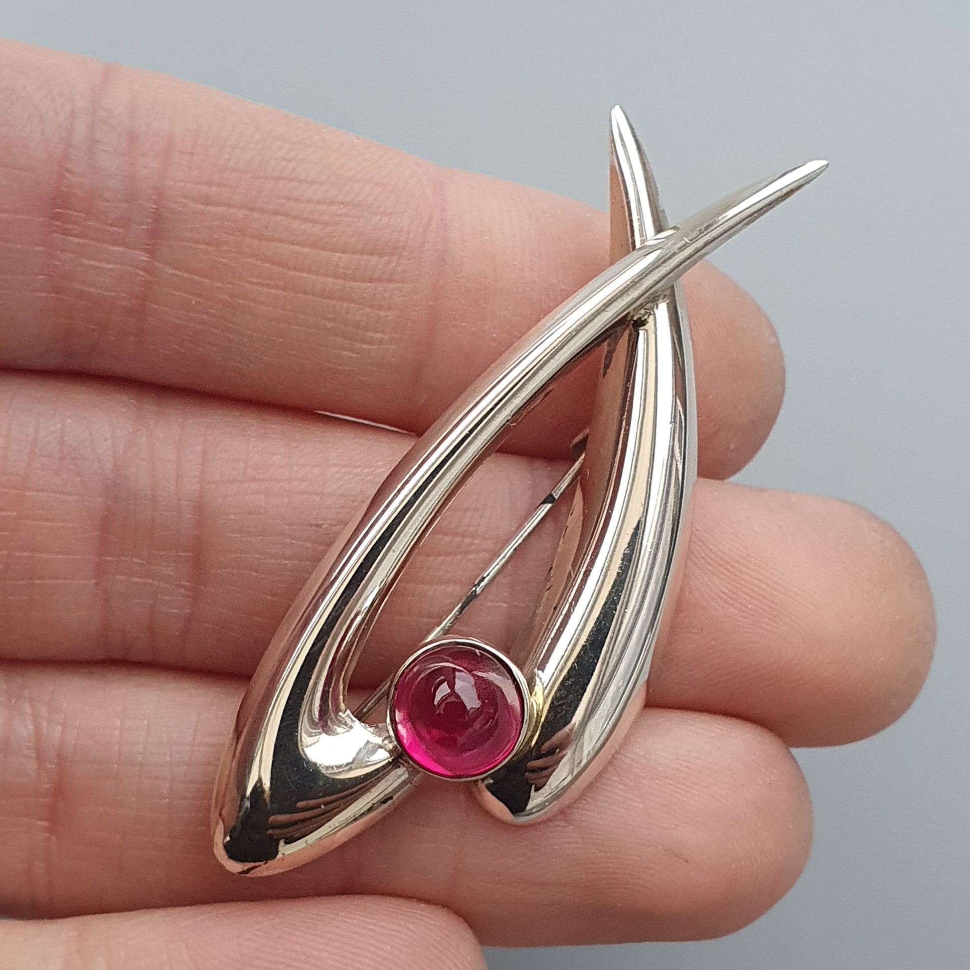 Silver pendant with an abstract teardrop shape featuring a red gemstone.