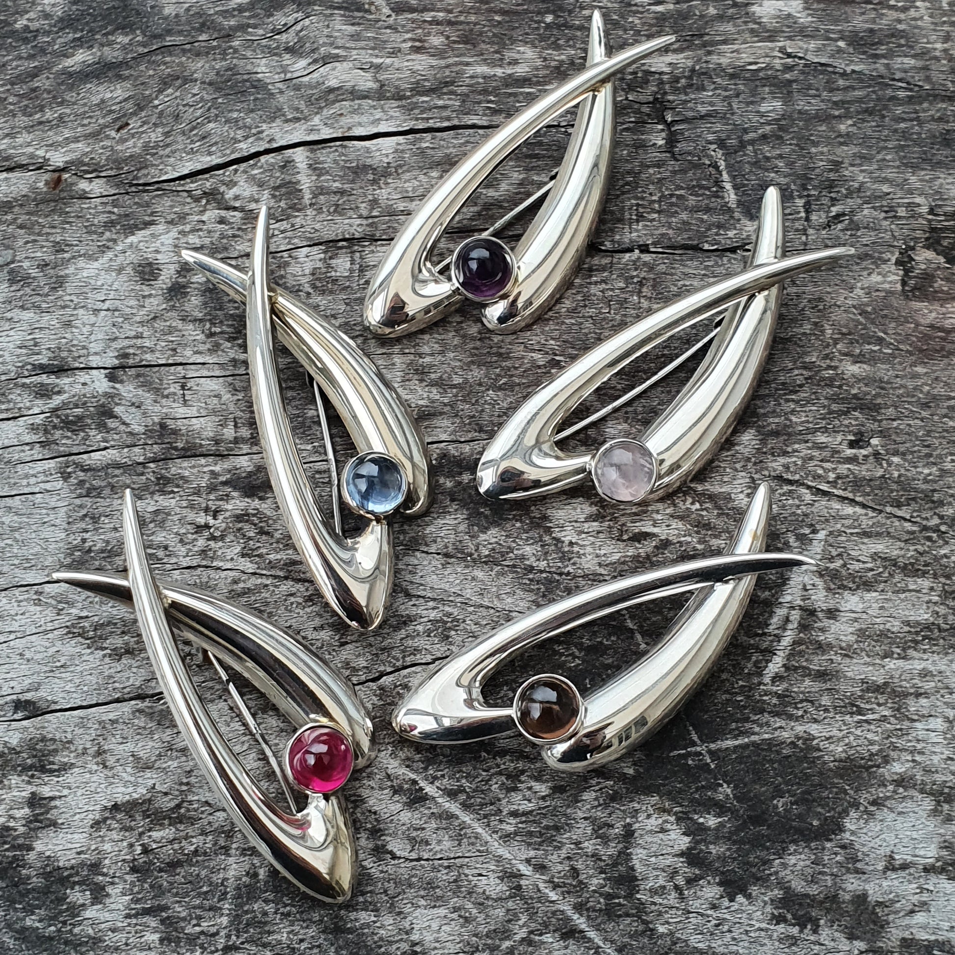 Silver fish-shaped pendants or brooches with colorful gemstones for eyes.