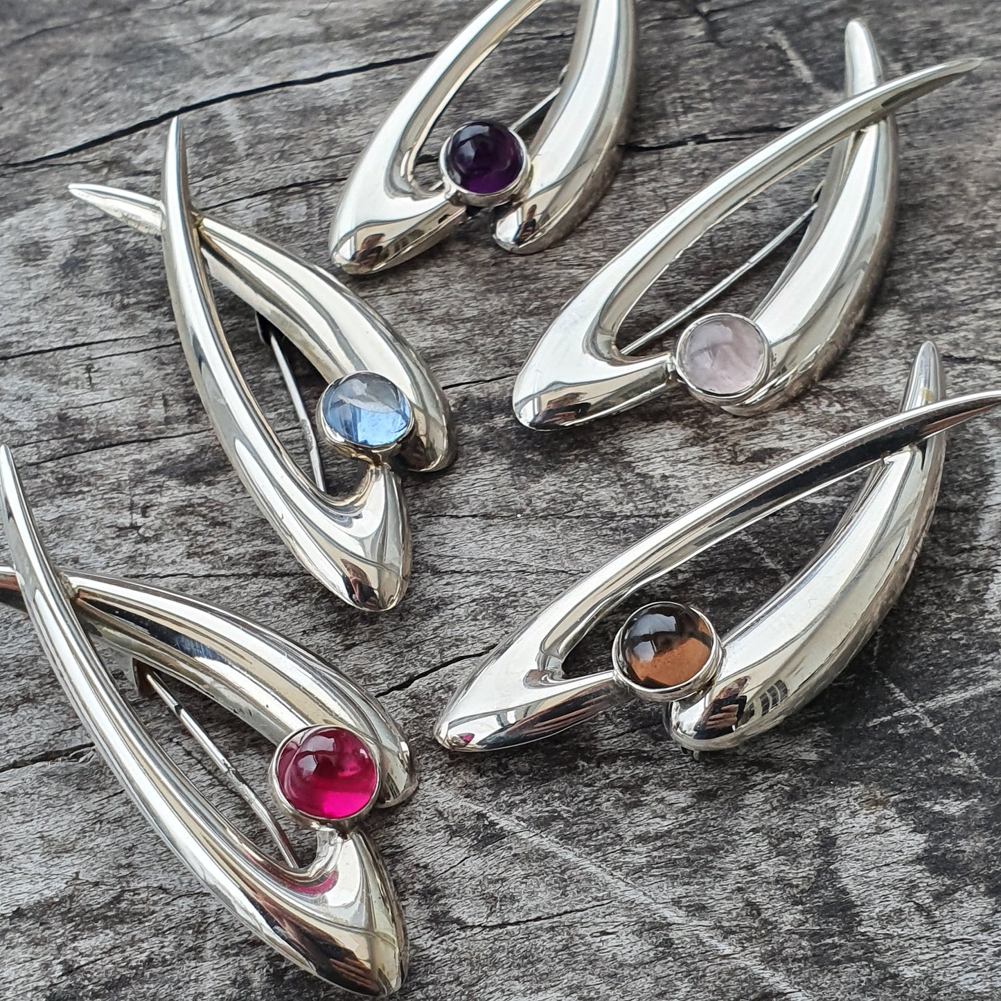 Silver pendants shaped like stylized fish or leaves, each set with a different colored gemstone.