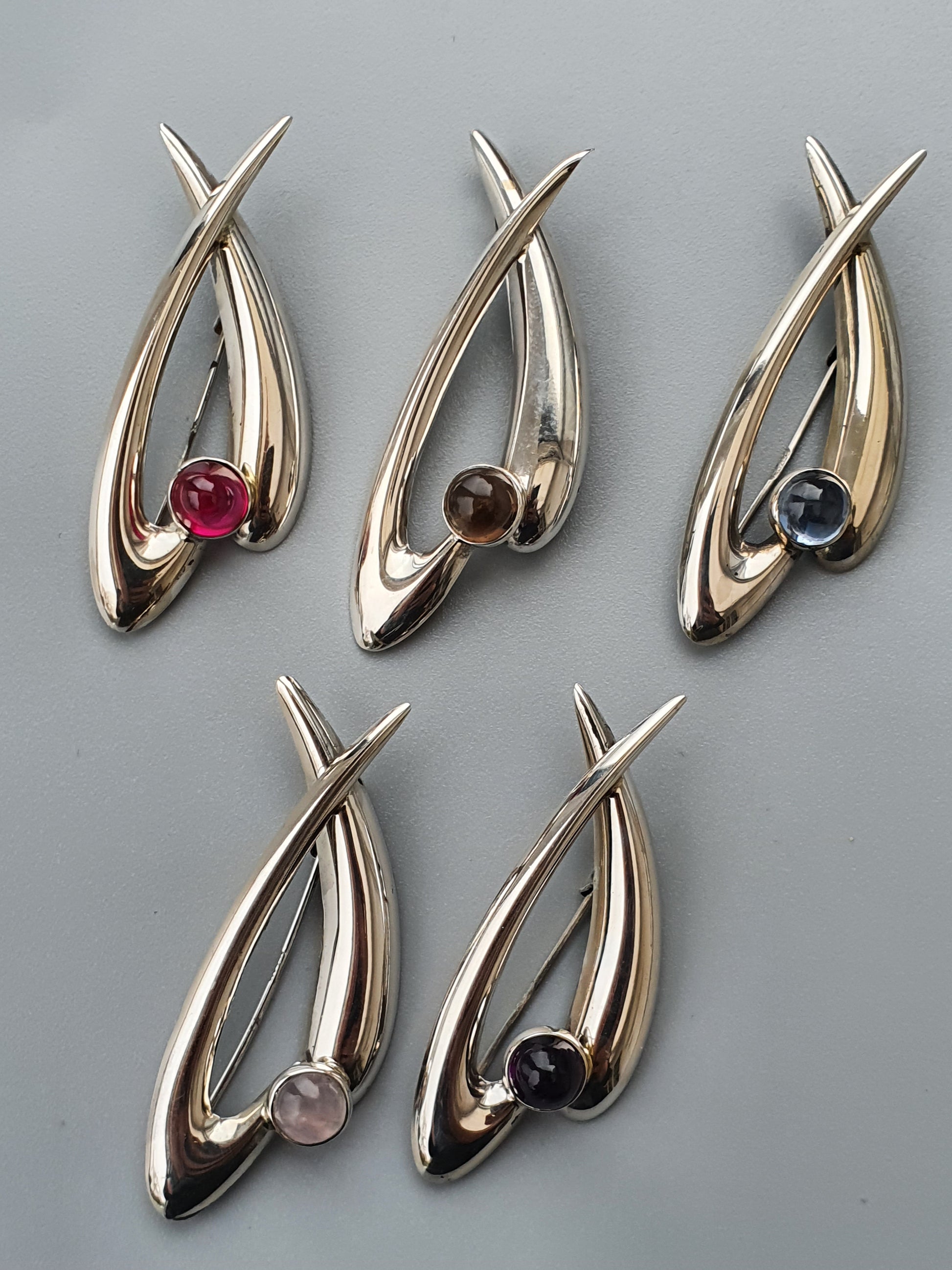 Metallic pendants with abstract teardrop shapes and colored gemstones.