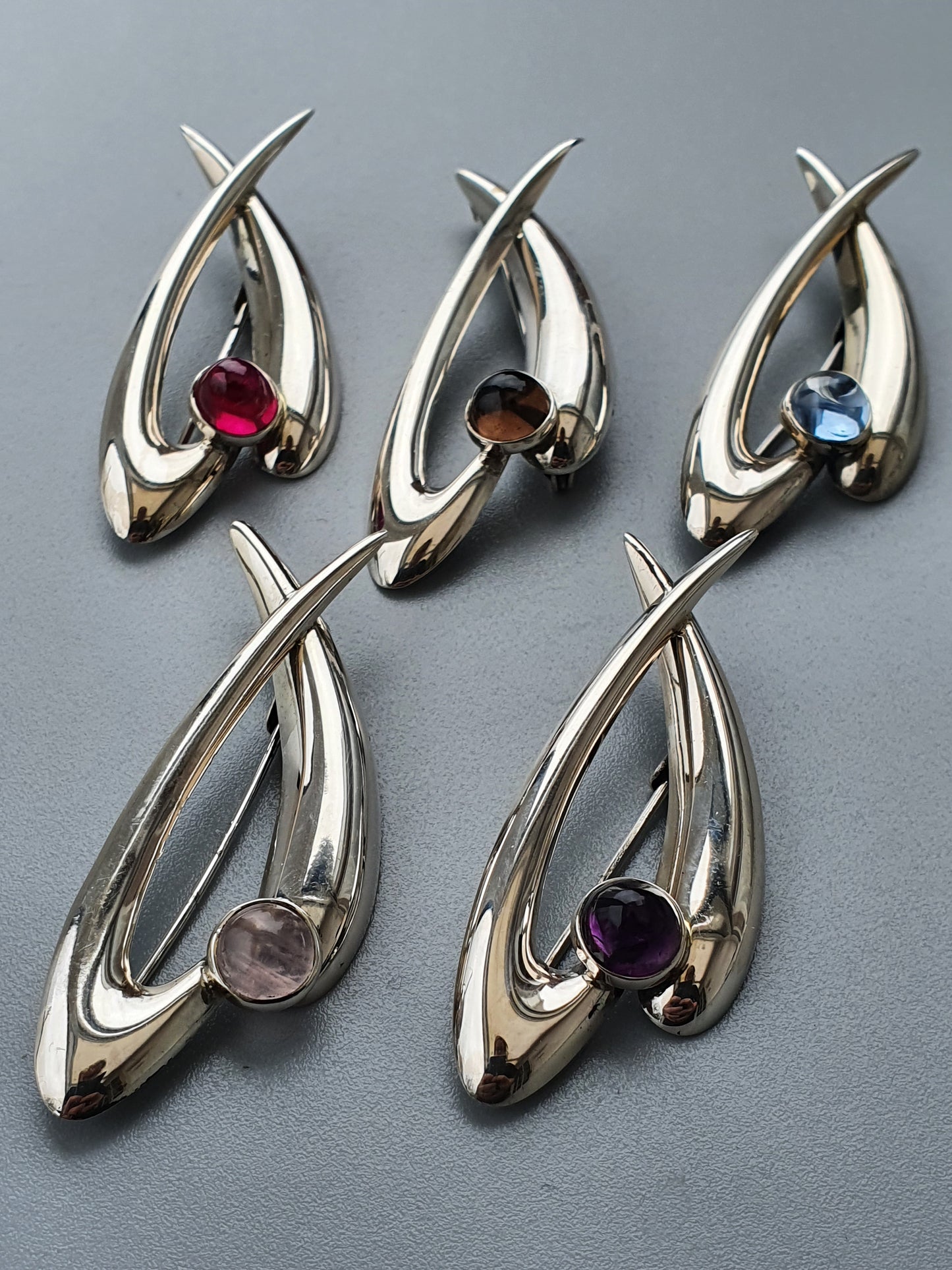 Silver-toned abstract pendants with colored gemstones set within curved metallic forms.