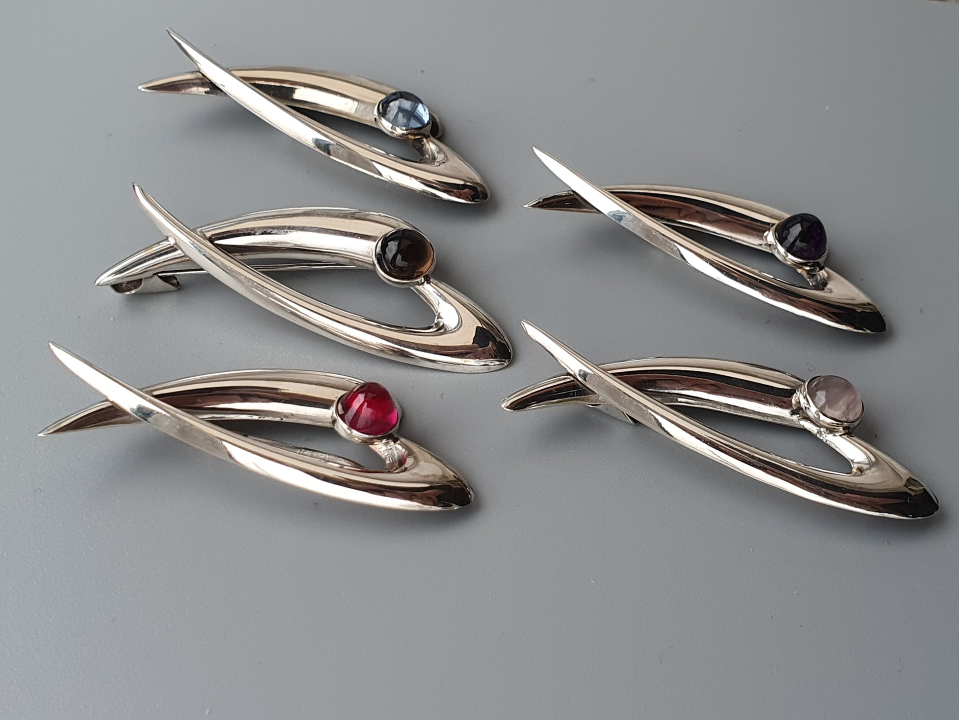 Sleek, fish-shaped silver brooches with colorful gemstone accents.