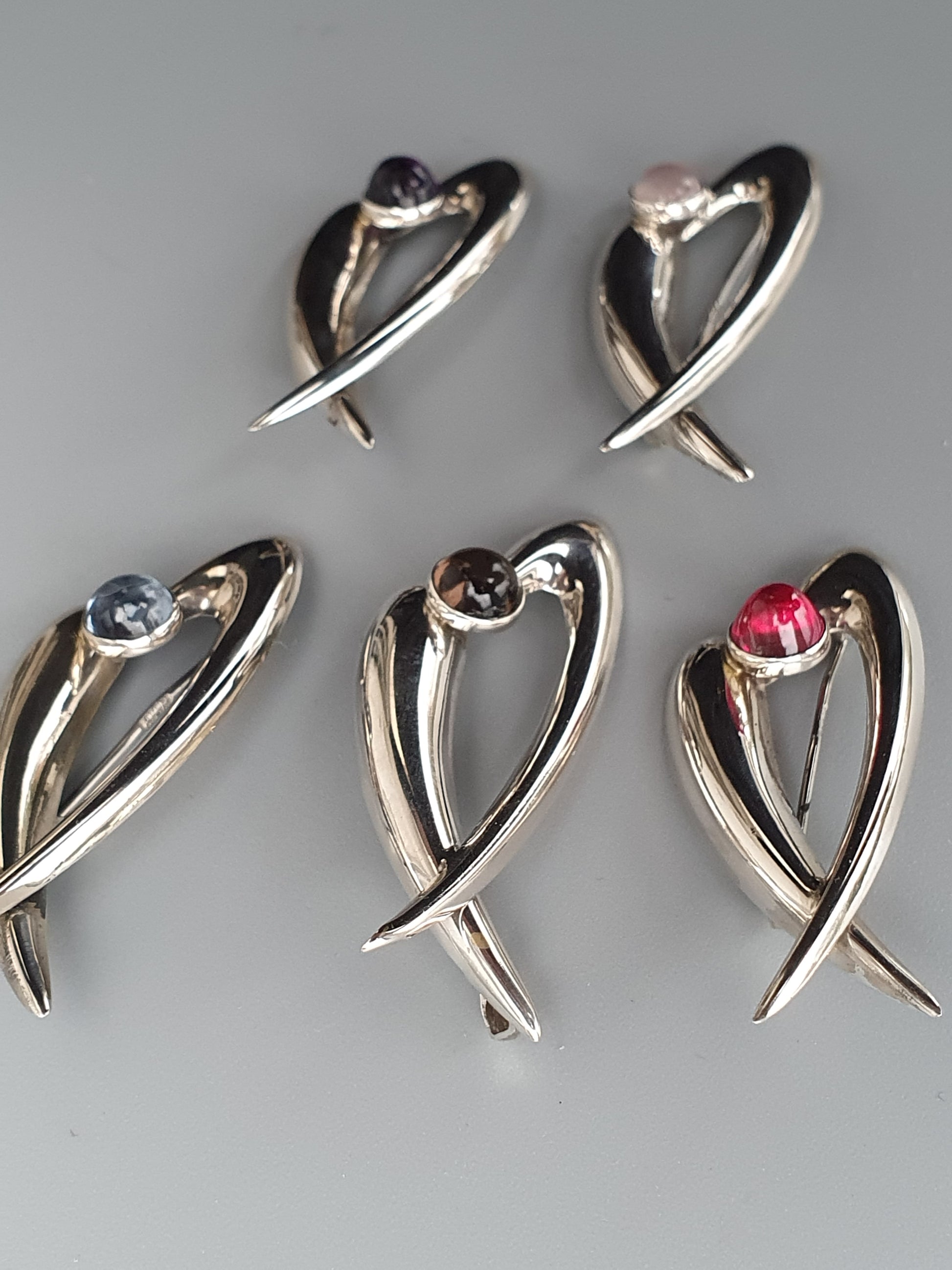 Heart-shaped silver brooches or pins with gemstone accents.