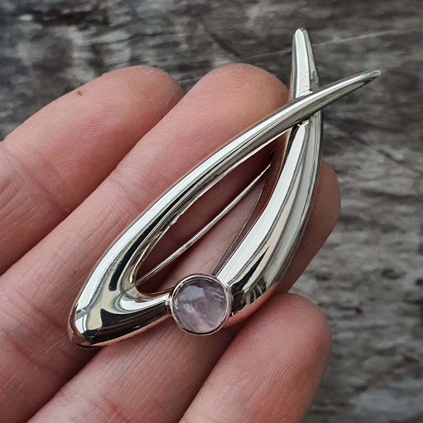 Sleek silver brooch with an oval design and a small round gemstone.