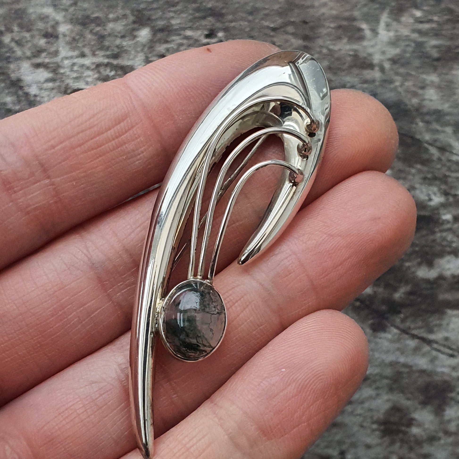 Silver brooch or pin with an abstract curved design and a small gemstone.