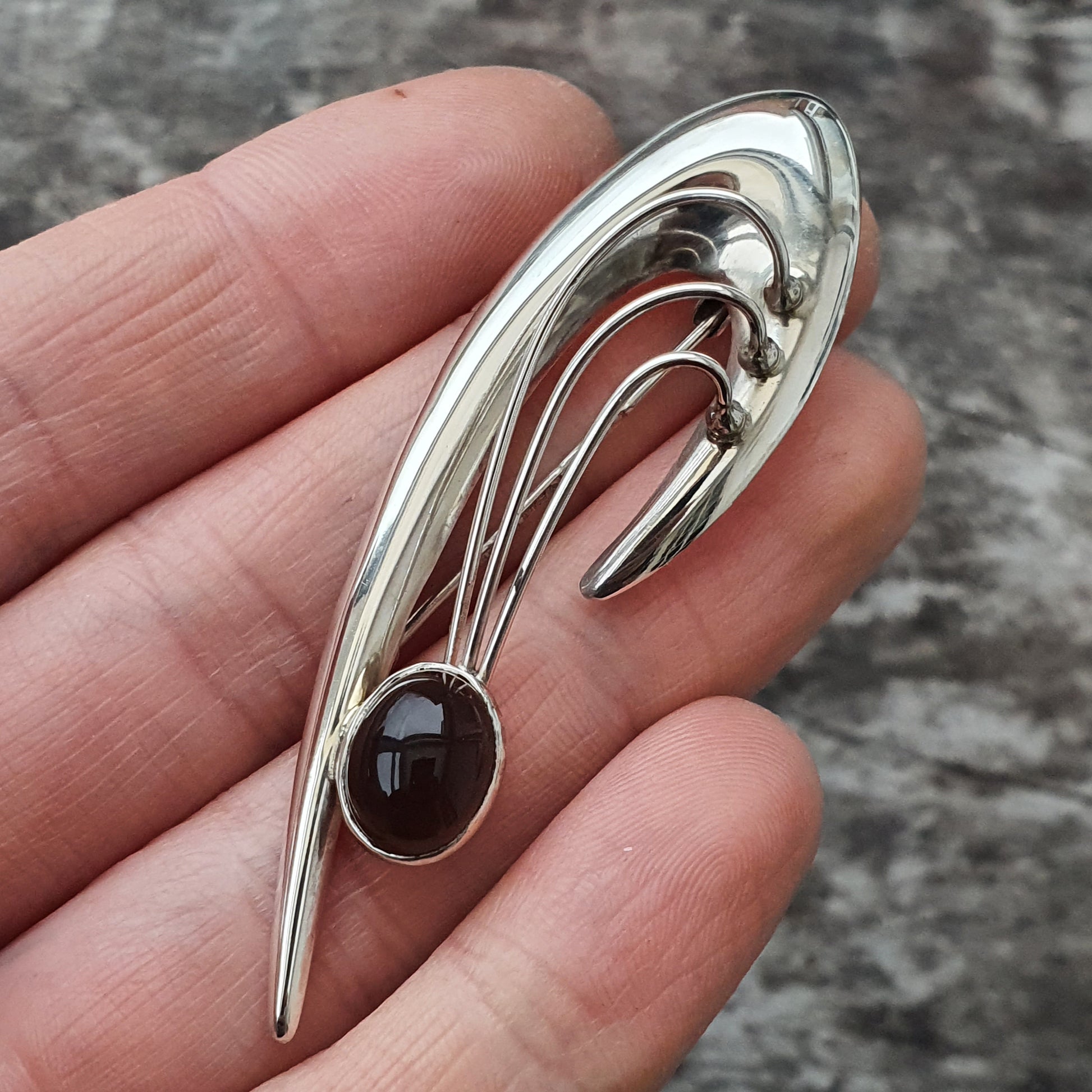 Silver brooch or pin with a curved design and a dark gemstone.