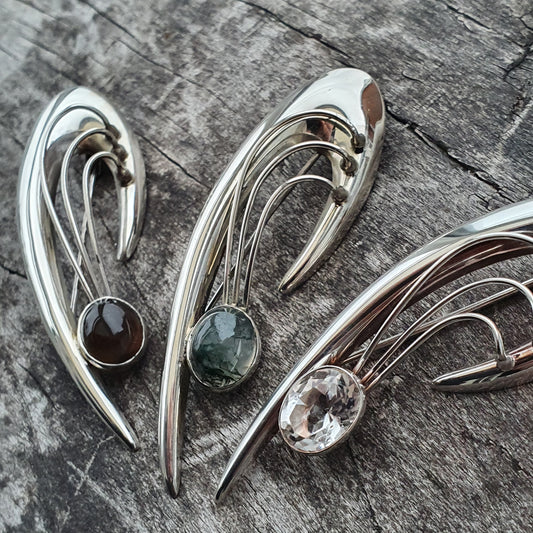 Elegant silver brooches or pins with curved designs and gemstone accents.