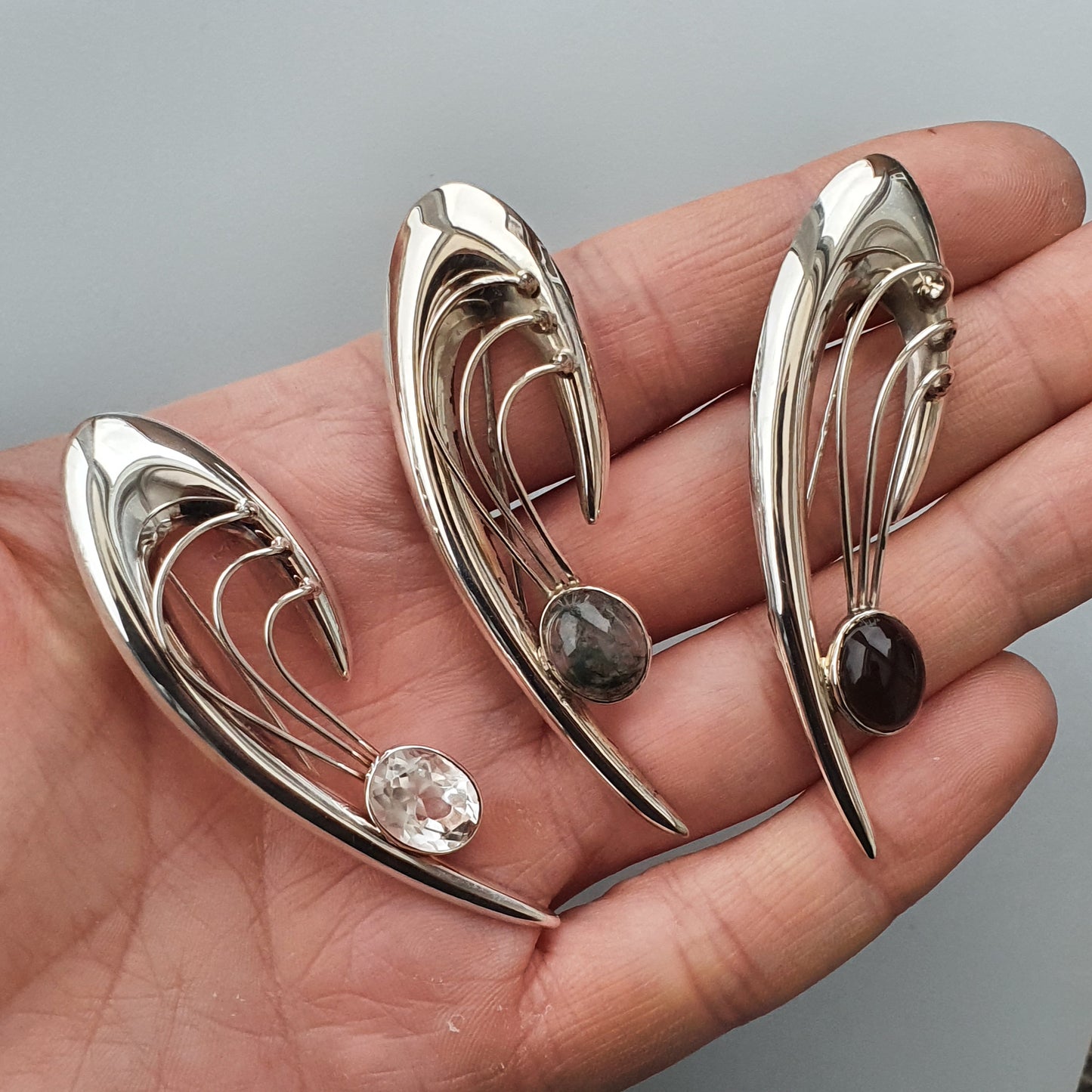 Sleek, curved silver brooches or pins with gemstone accents.