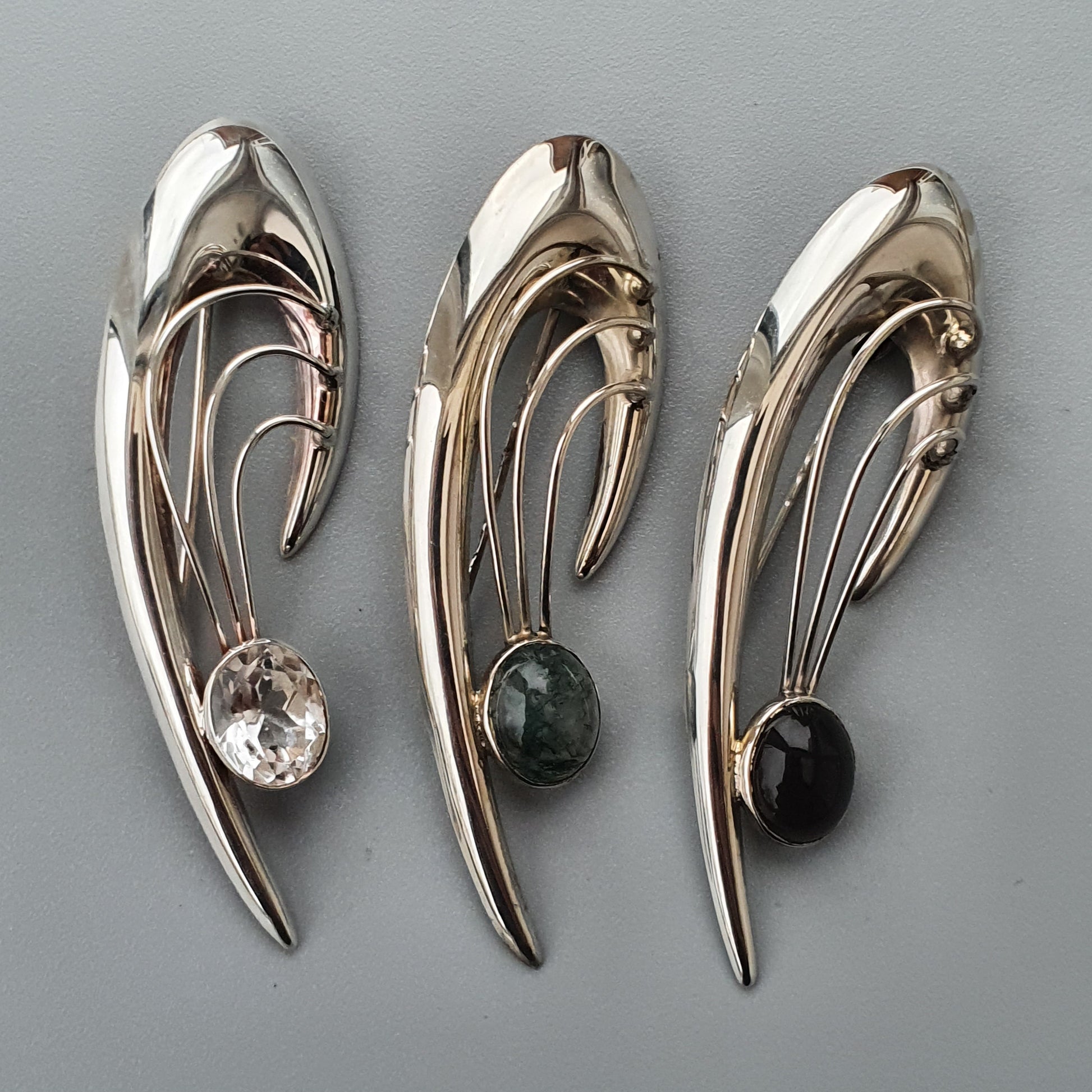 Three elegant, curved metallic brooches with gemstone accents.