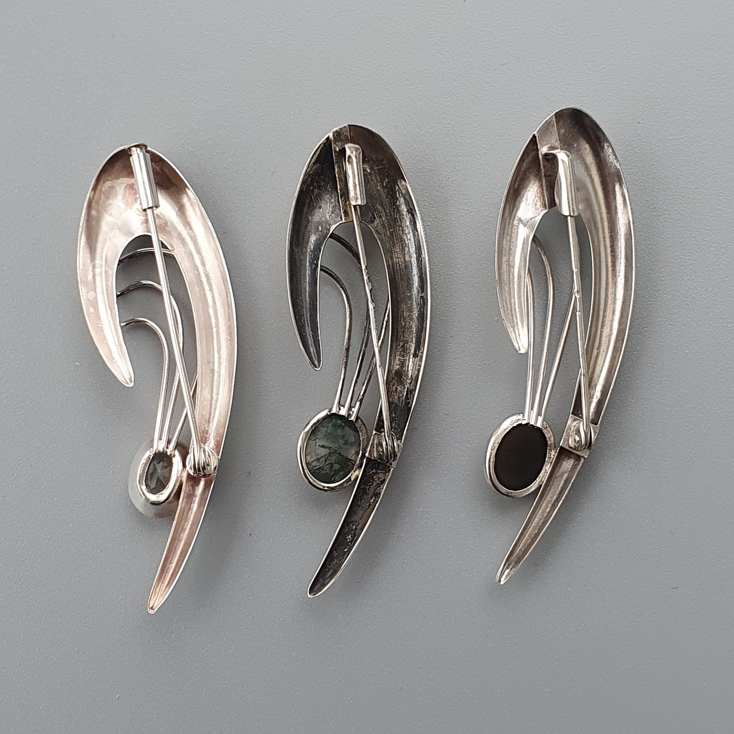 Three metallic ear cuffs or ear wraps with curved, abstract designs and small gemstone accents.