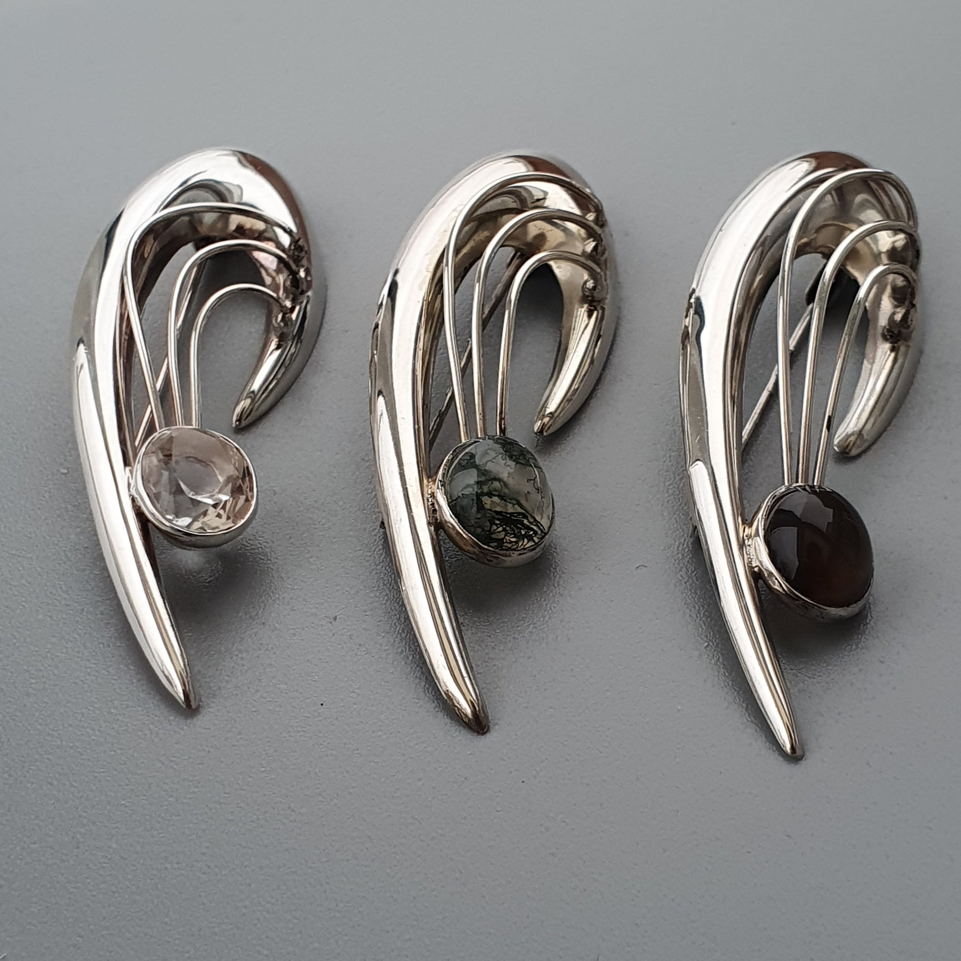 Three silver-toned abstract brooches with curved shapes and gemstones.