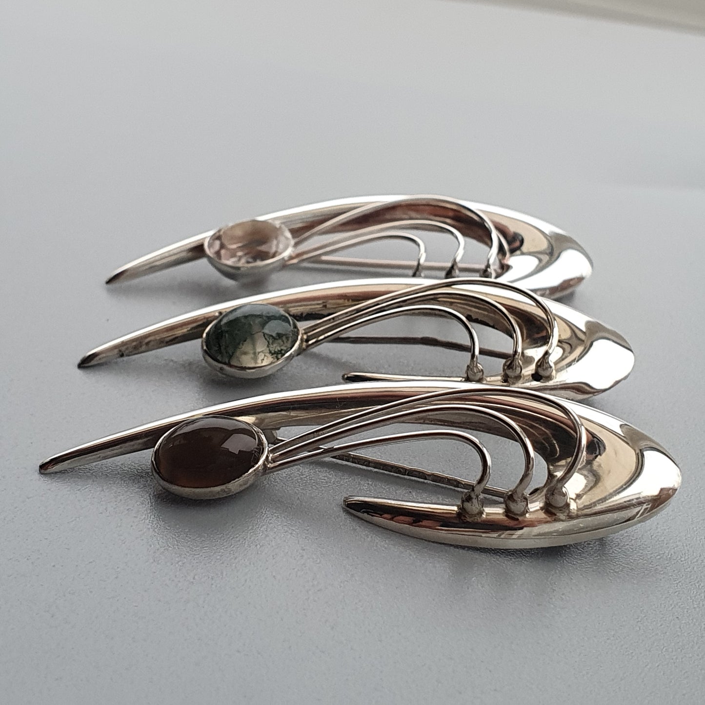 Set of three silver-toned brooches with curved shapes and inset gemstones.