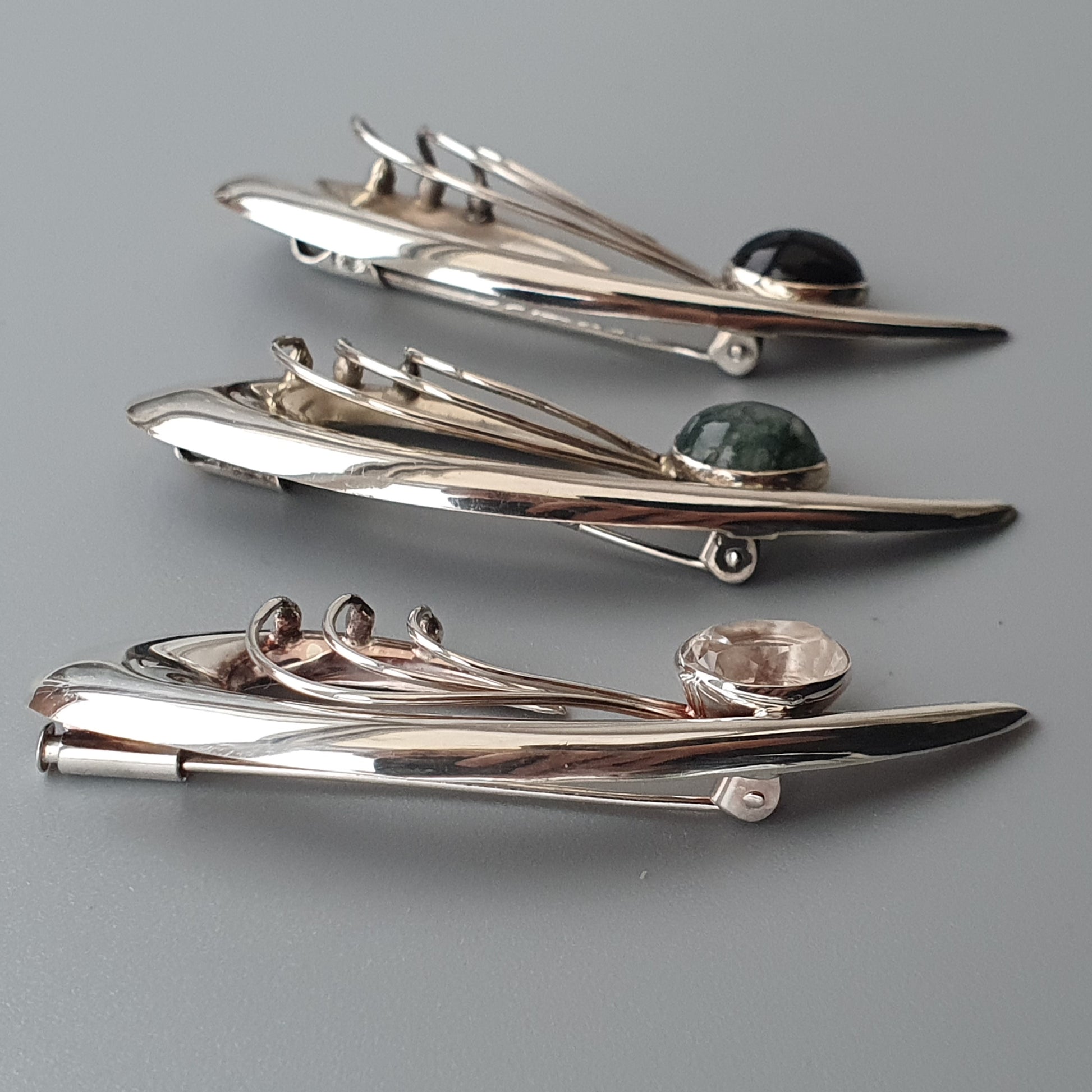 Sleek, retro-futuristic silver brooches shaped like stylized spacecraft or rockets.