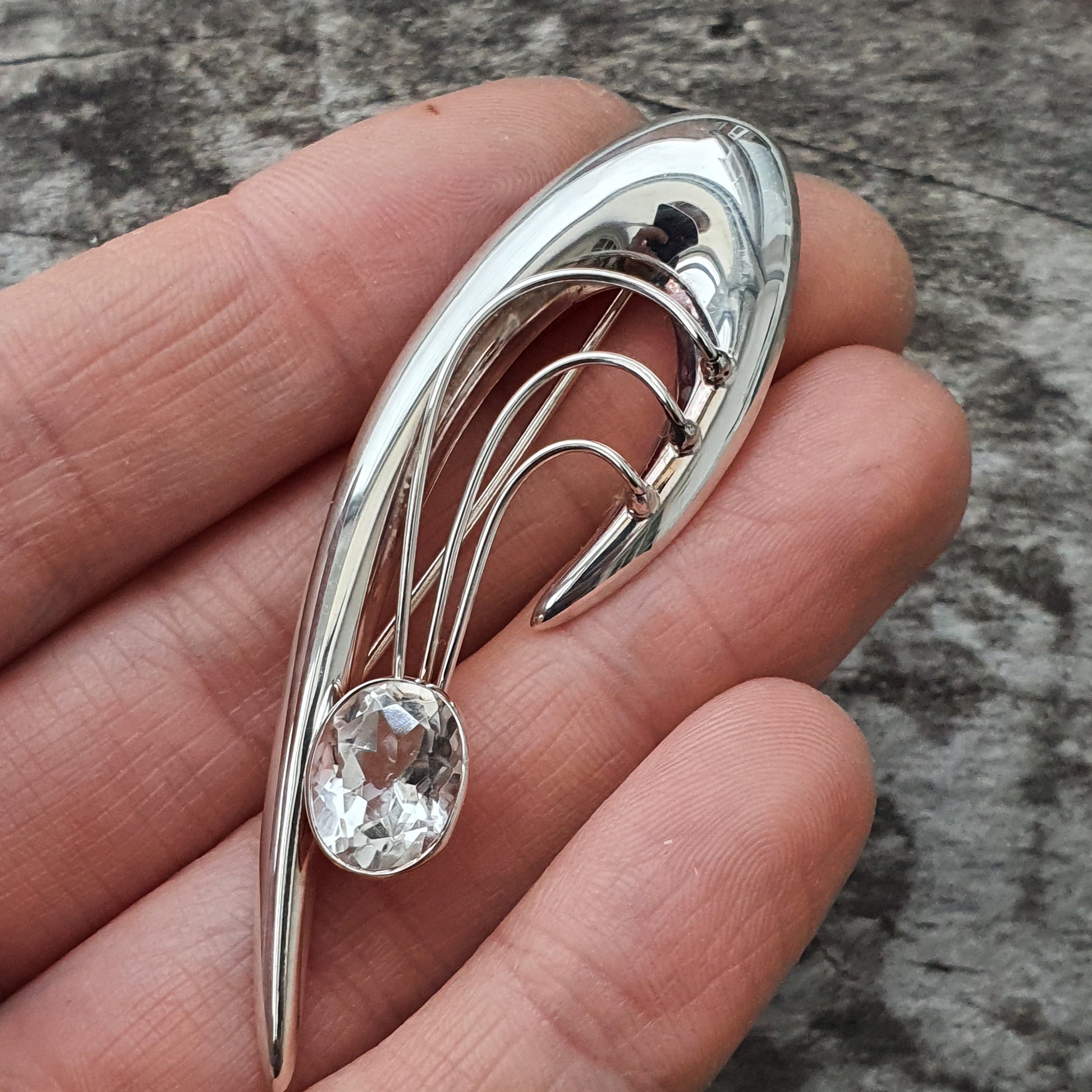 Elegant silver brooch with curved lines and a clear gemstone.