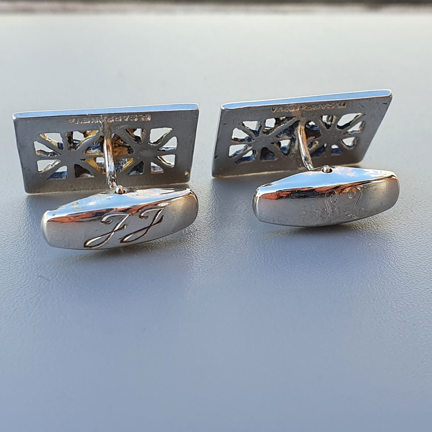 Pair of silver cufflinks with decorative cutout patterns and engraved initials.