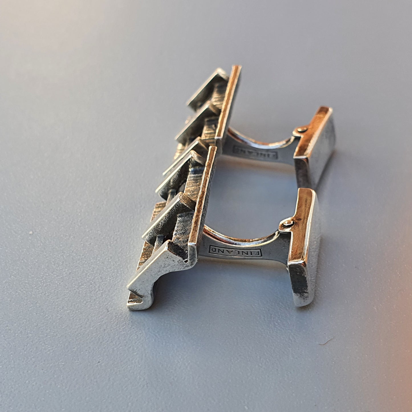 Metal cufflink with an architectural design resembling a bridge or building structure.