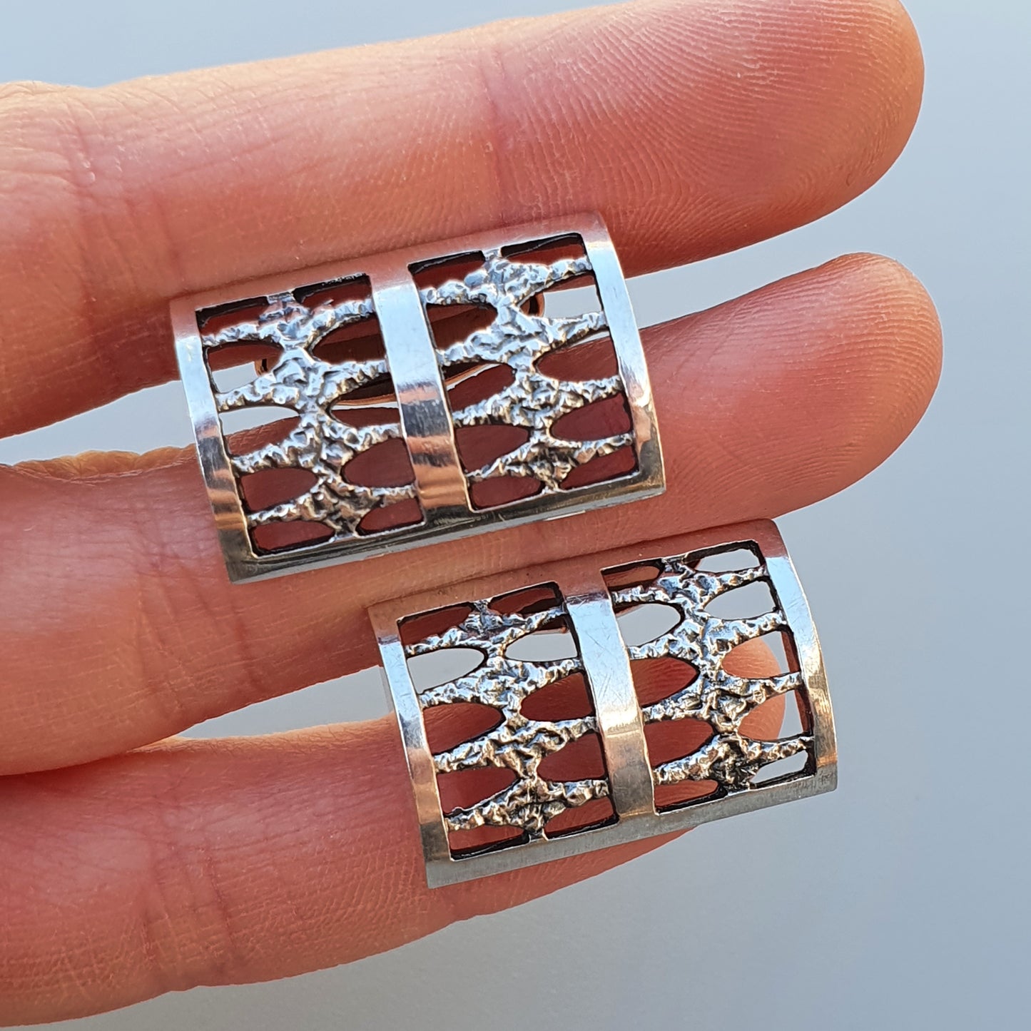 Pair of silver-colored cylindrical jewelry pieces with intricate snowflake or tree-like cutout designs.