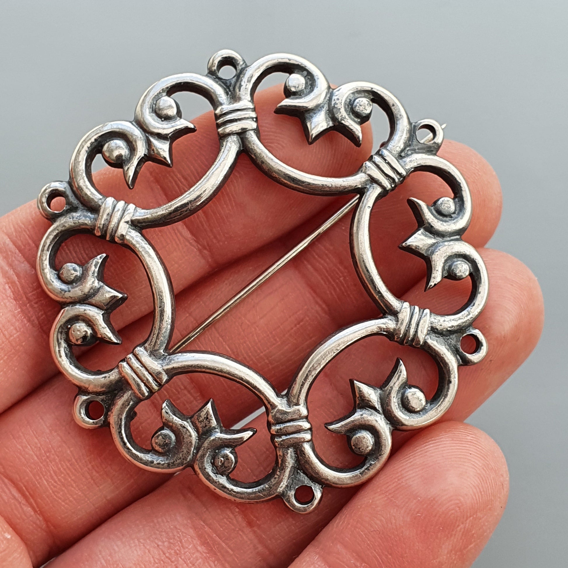 Ornate silver brooch with swirling filigree design and heart-shaped elements.