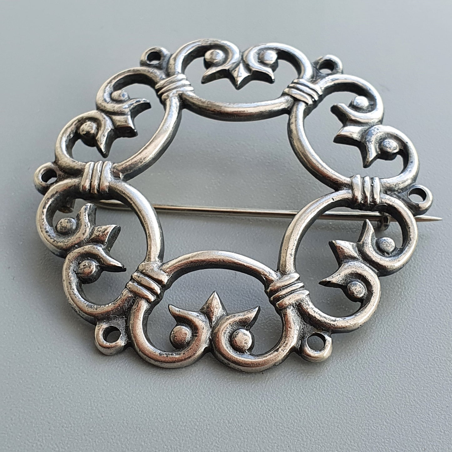 Ornate silver brooch with intricate scrollwork design.