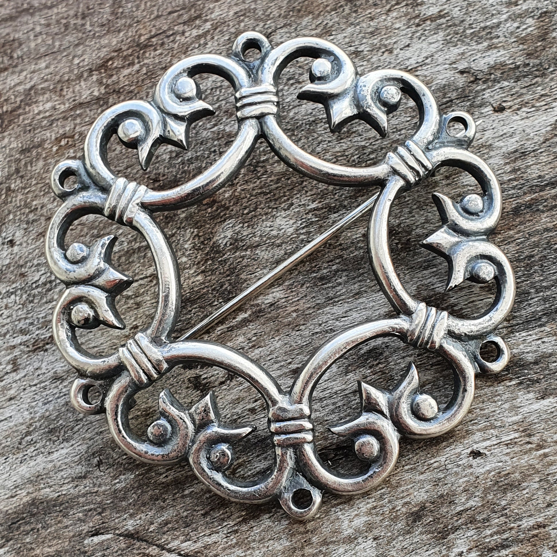 Ornate silver brooch with intricate swirling patterns forming a circular design.