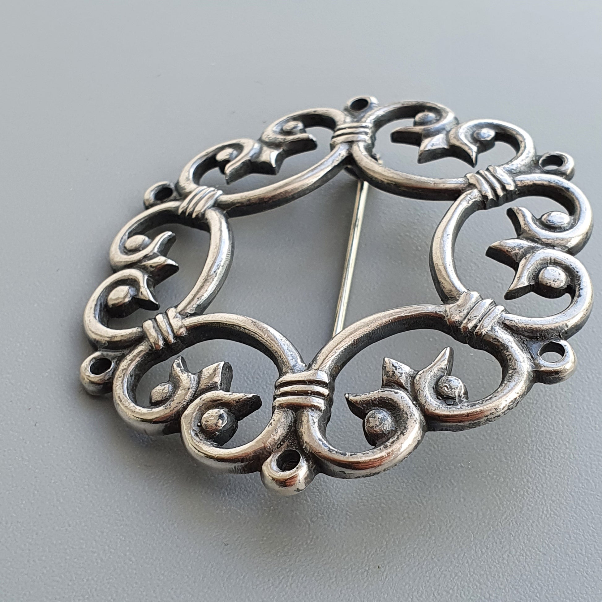 Ornate silver brooch with intricate swirling patterns and floral motifs.