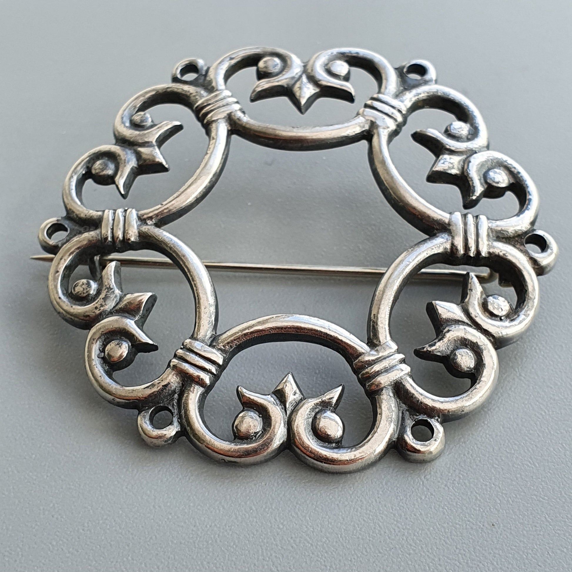 Ornate silver brooch with intricate swirling patterns forming a circular design.