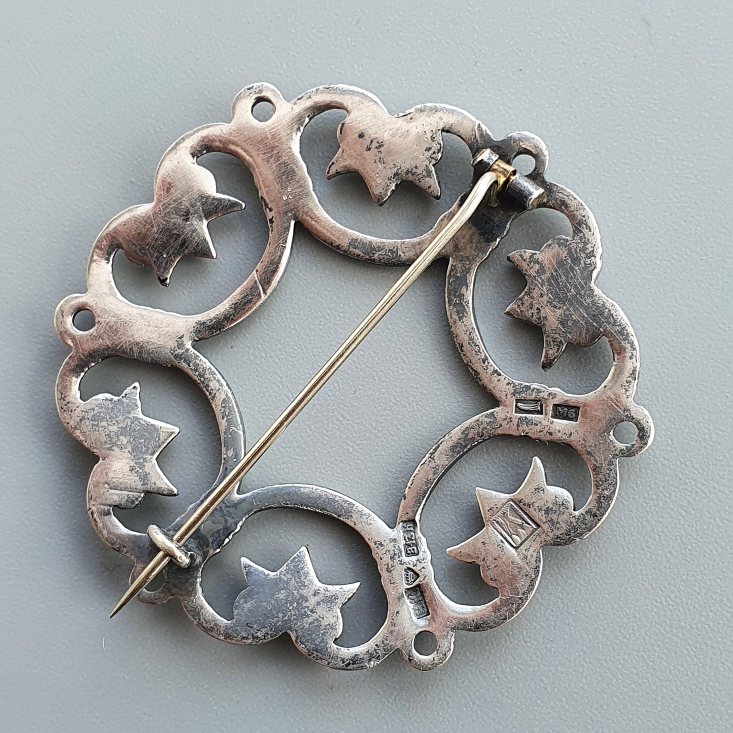 Circular silver brooch with star and crescent moon shapes connected in a decorative pattern.