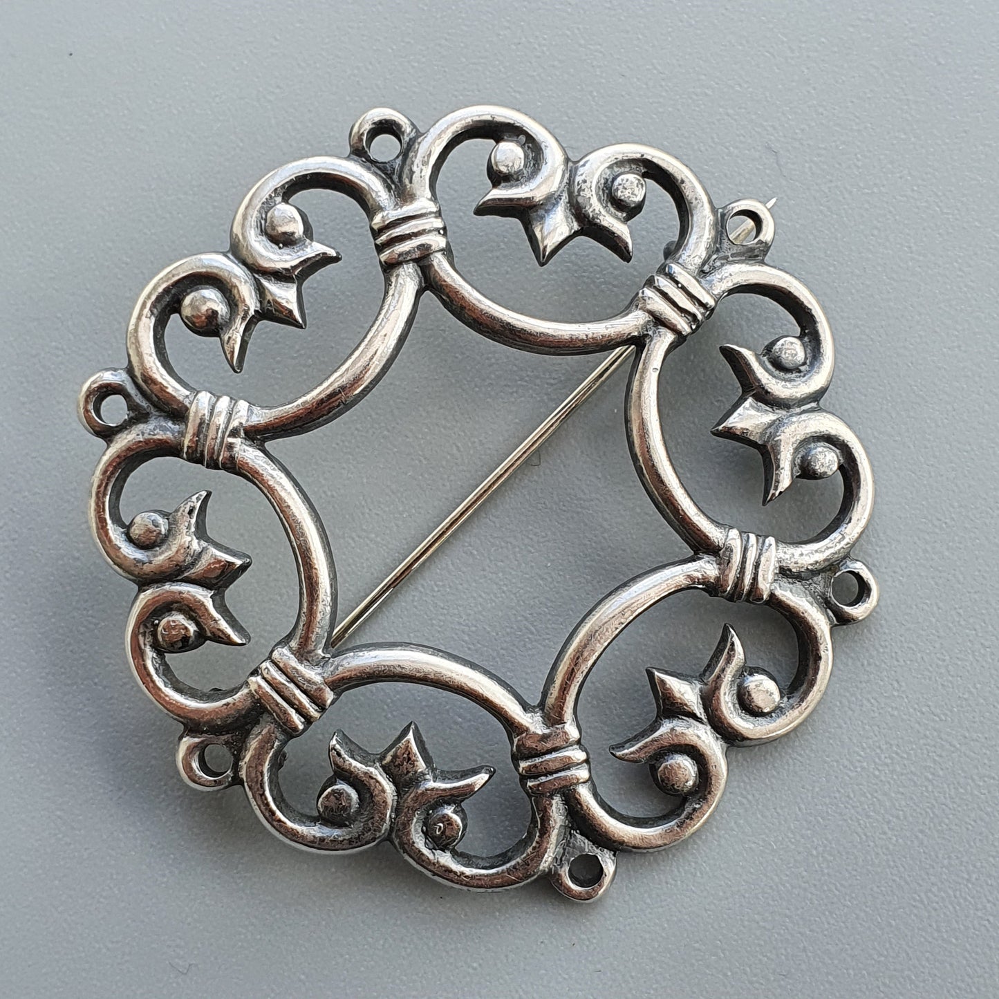 Ornate silver brooch with swirling floral designs and star-shaped accents.