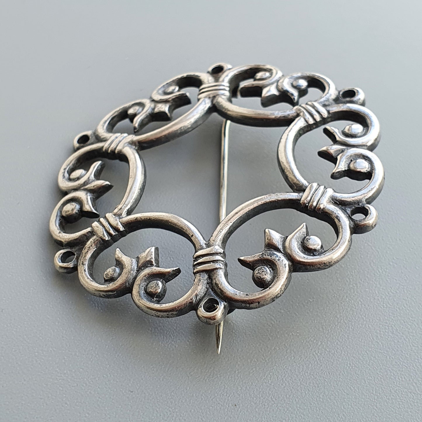 Ornate silver brooch with intricate swirling patterns and scrollwork design.