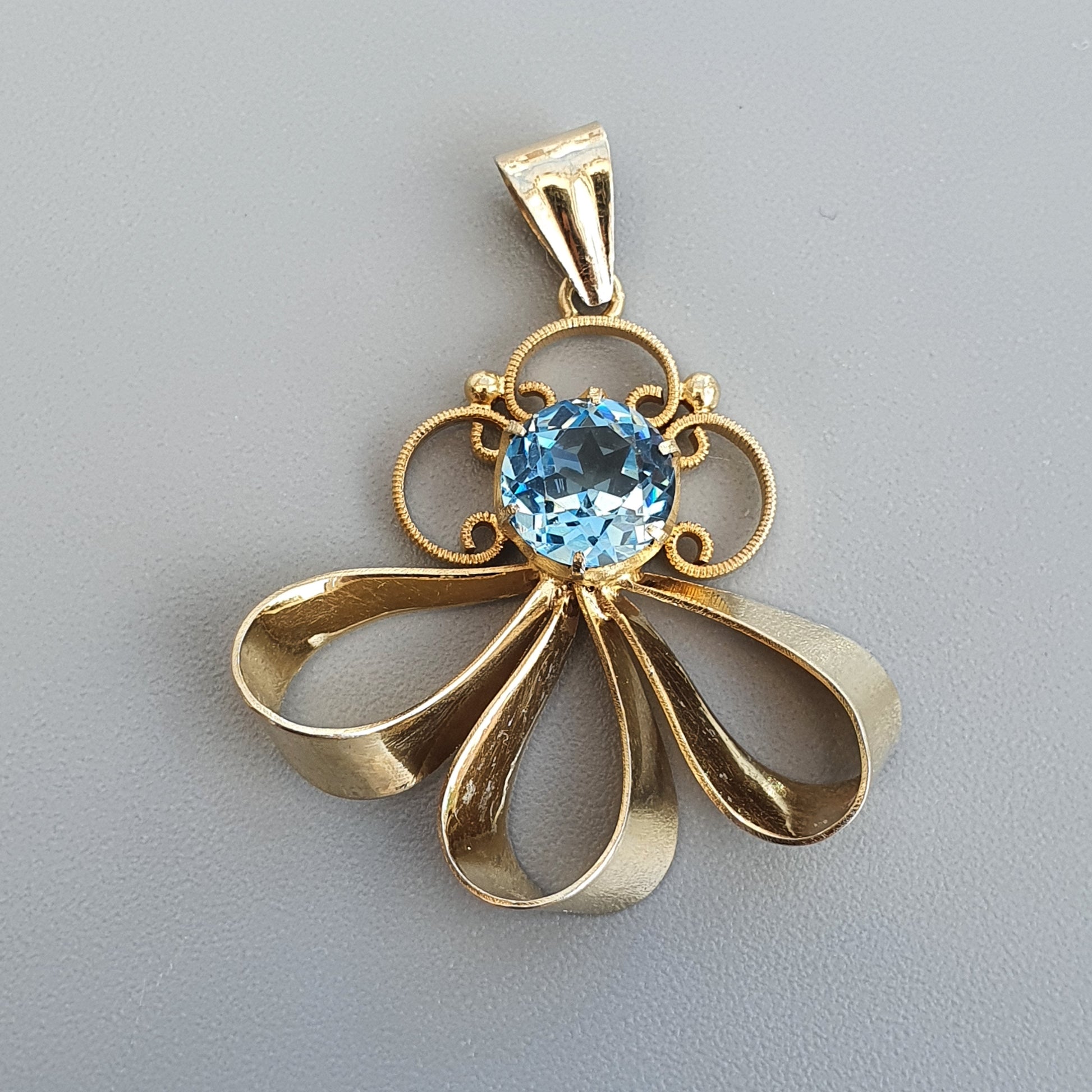 Gold pendant featuring a flower-like design with a blue gemstone at its center.