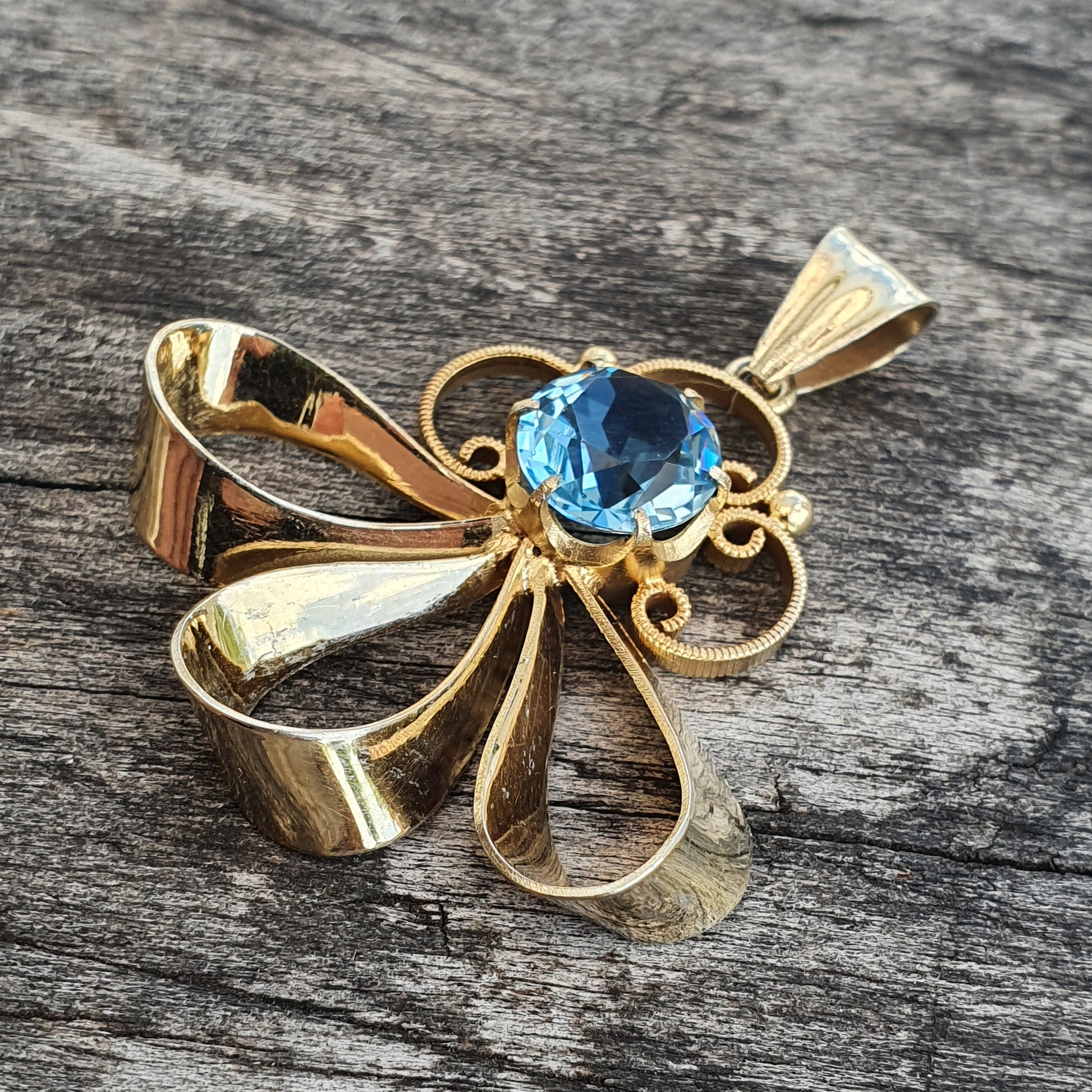 Gold bow-shaped pendant featuring a blue gemstone centerpiece.