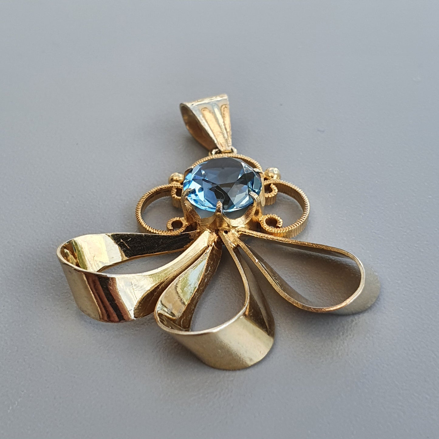 Gold pendant featuring a blue gemstone and a bow-like design.