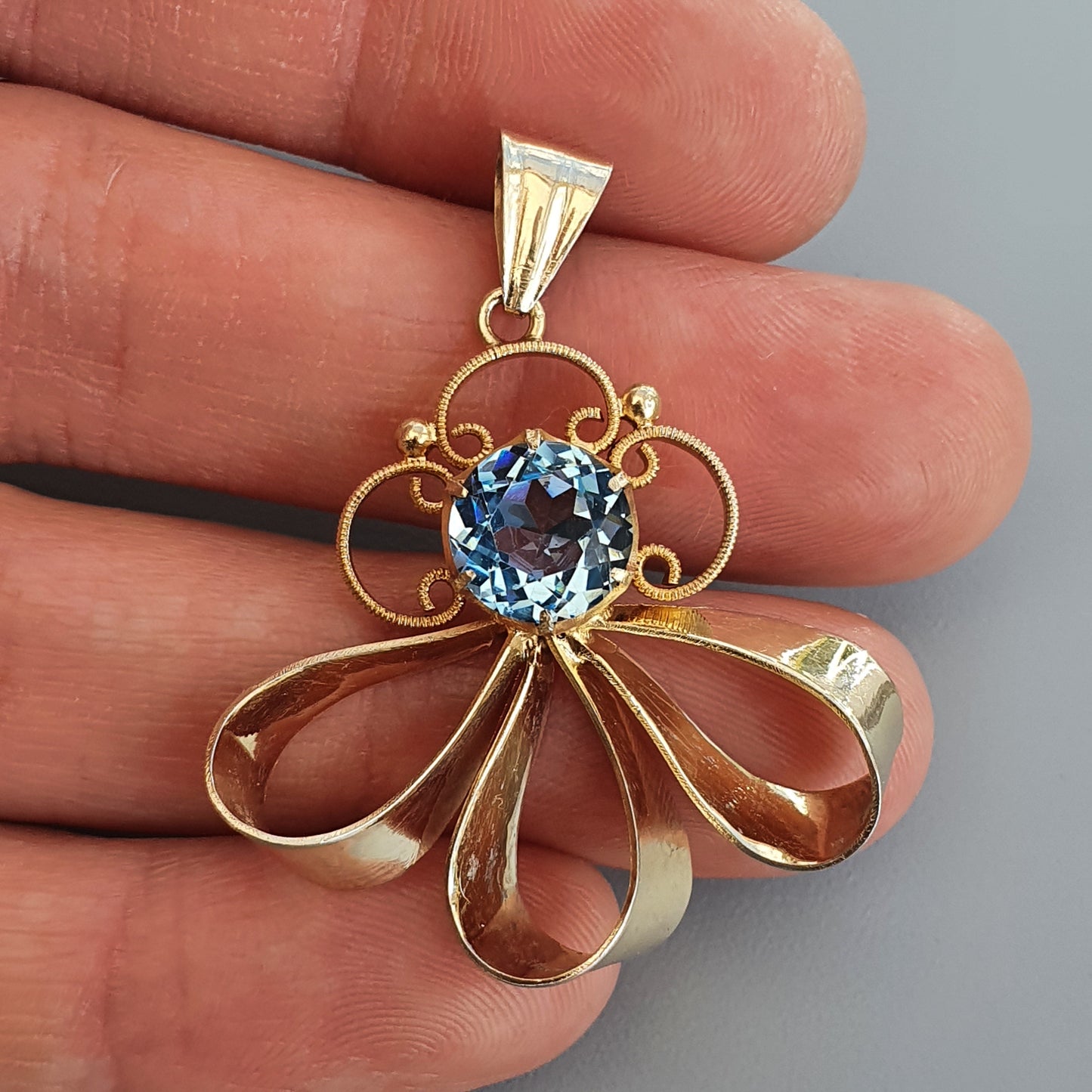 Gold pendant featuring a blue gemstone surrounded by a floral-inspired design.