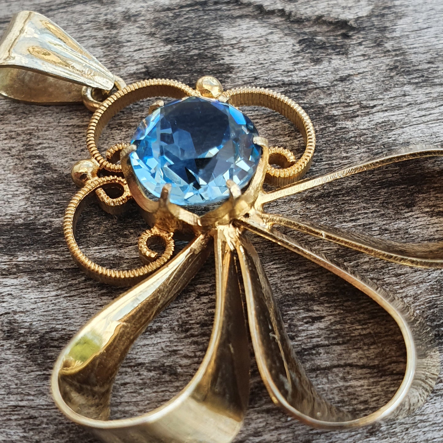 Gold pendant featuring a blue gemstone centerpiece with decorative loops and teardrop shapes.