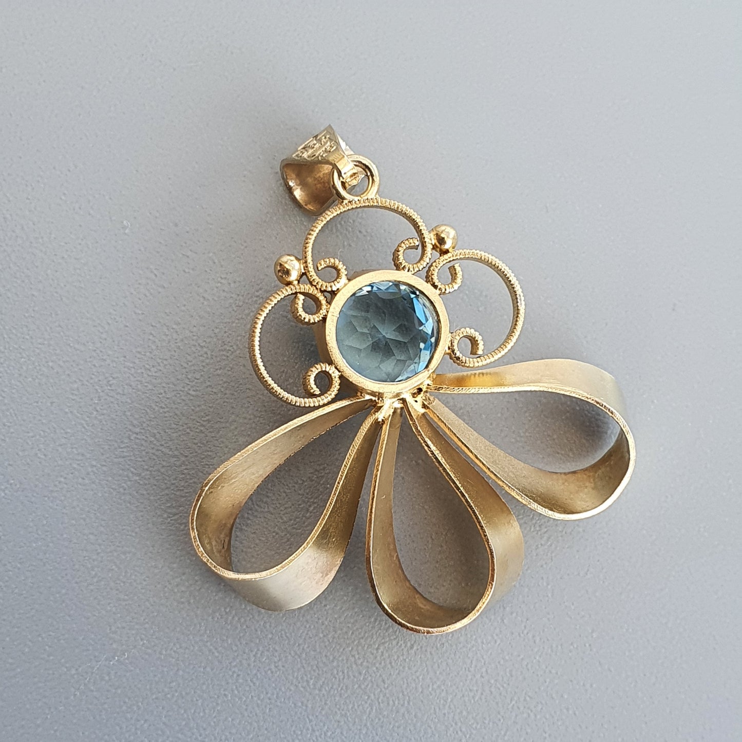 Gold pendant featuring a blue gemstone surrounded by swirling designs and petal-like shapes.