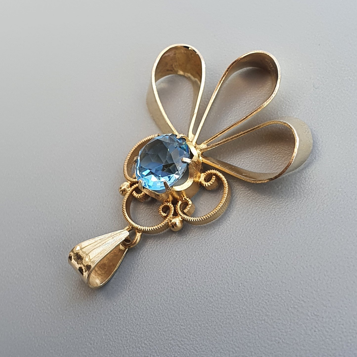 Decorative gold-toned brooch featuring a blue gemstone and floral petal design.