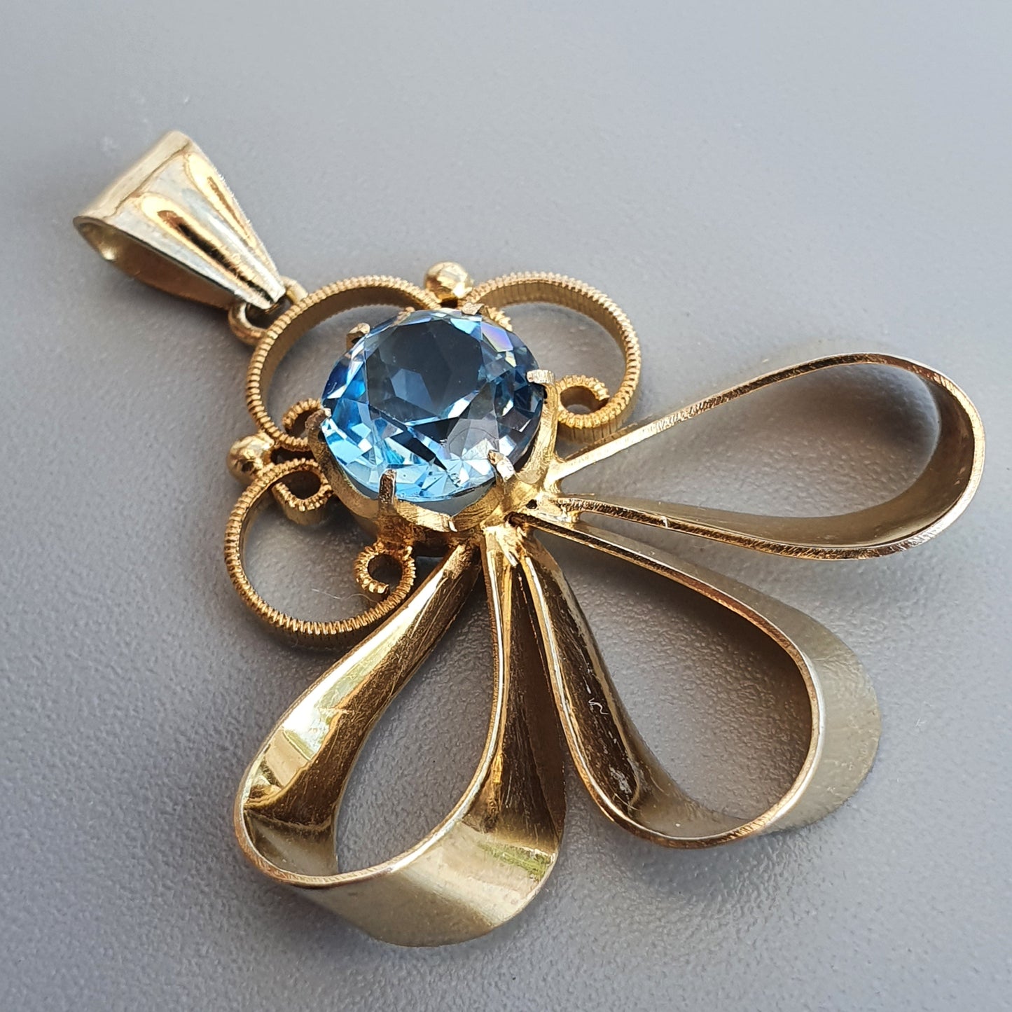 Gold pendant featuring a blue gemstone set in a stylized bow or flower design.