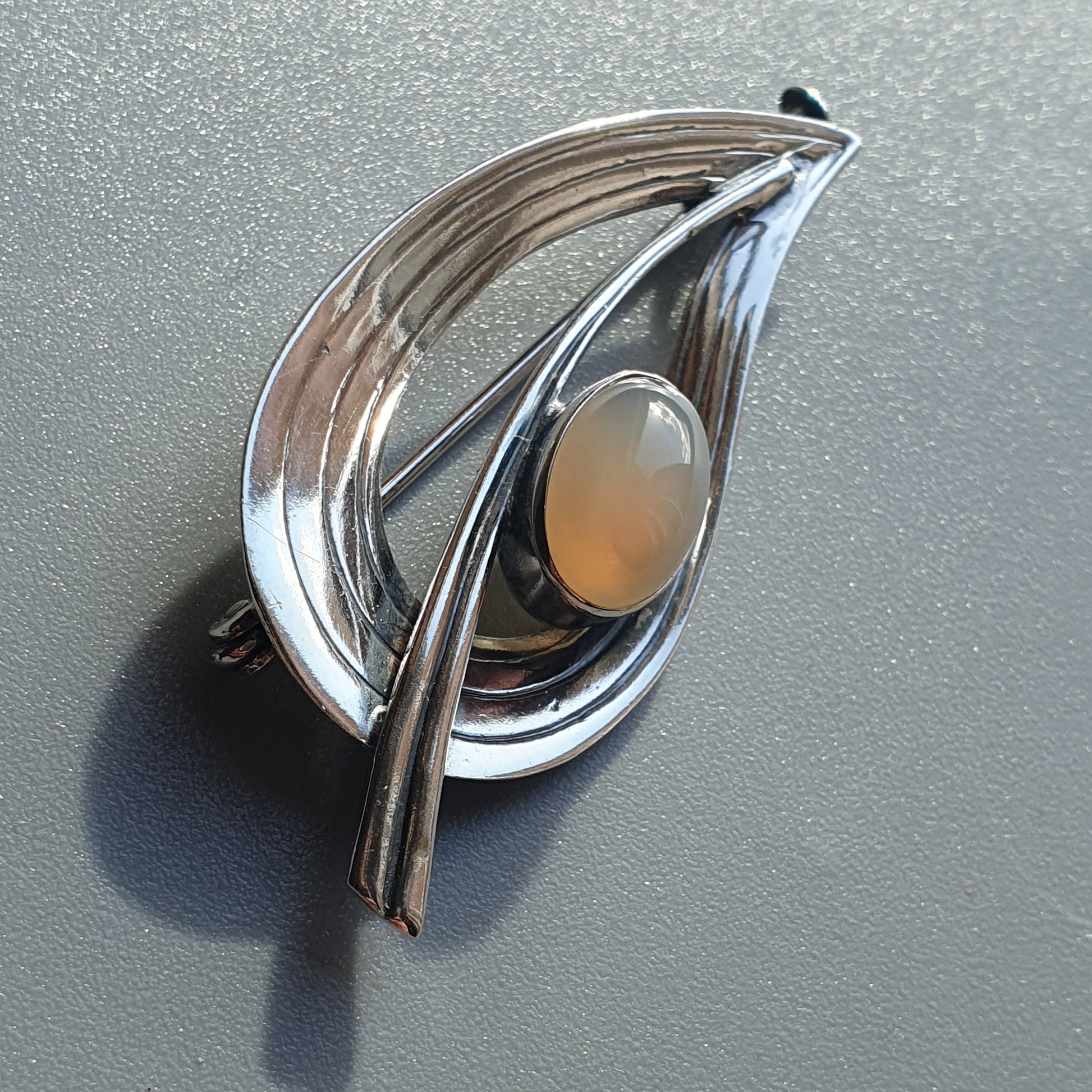 Stylized silver brooch with a teardrop shape and an opal-like stone centerpiece.