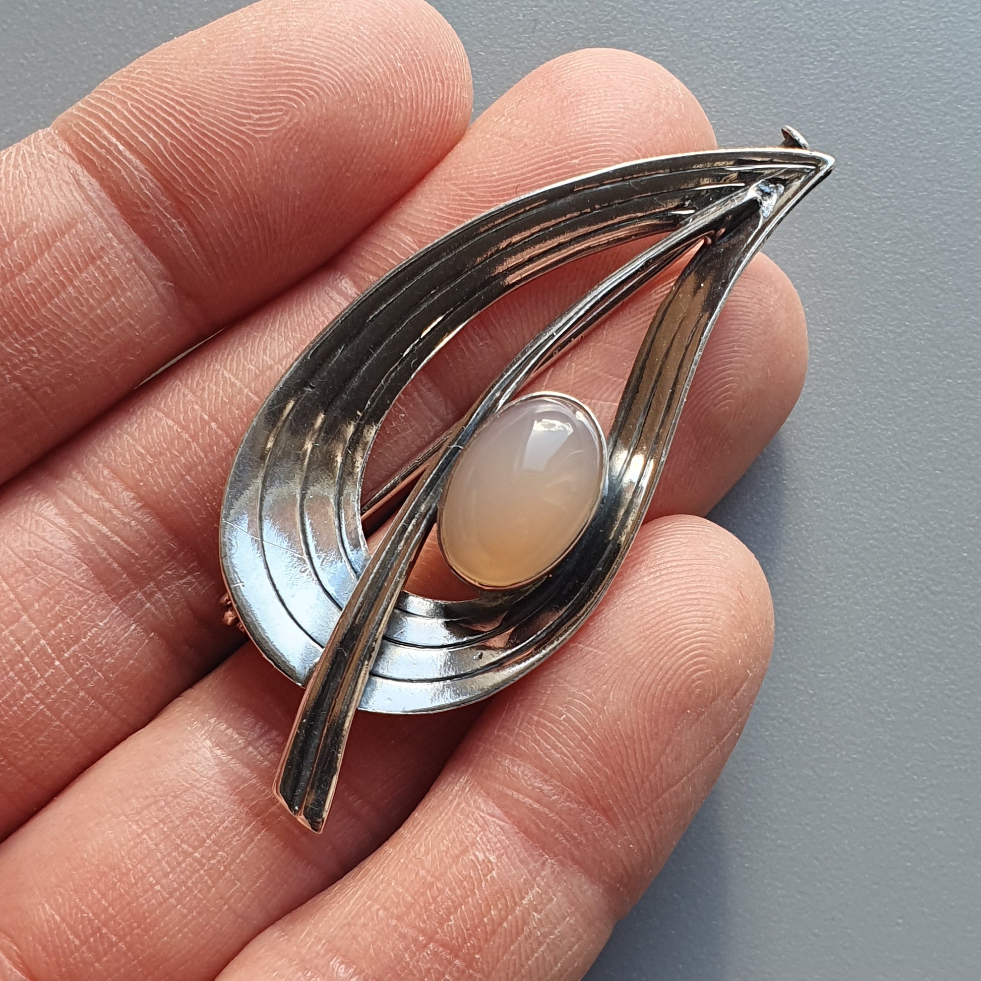 Teardrop-shaped silver brooch with a pearlescent stone in the center.