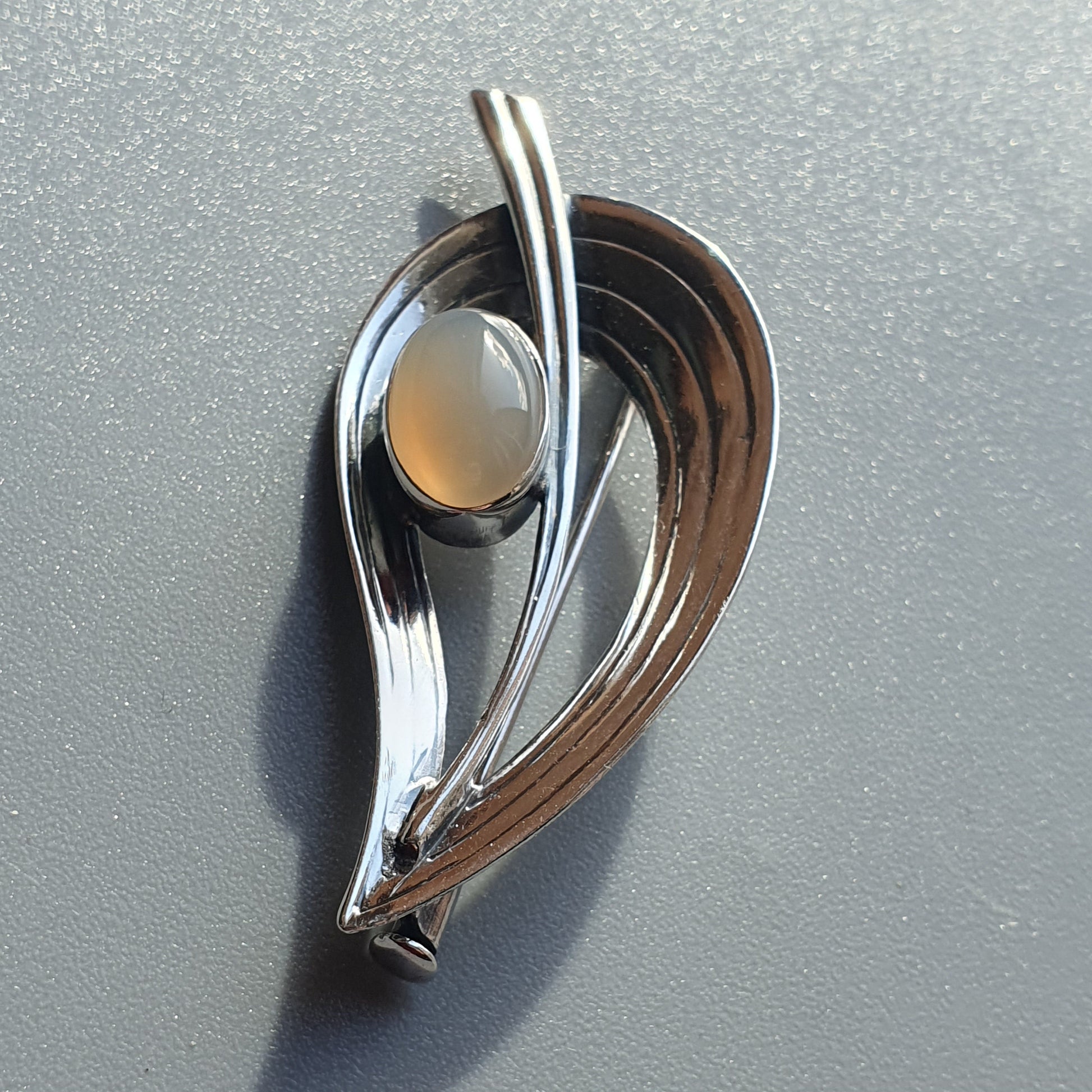 Sleek silver brooch or pendant with a teardrop shape and inset pearl-like stone.