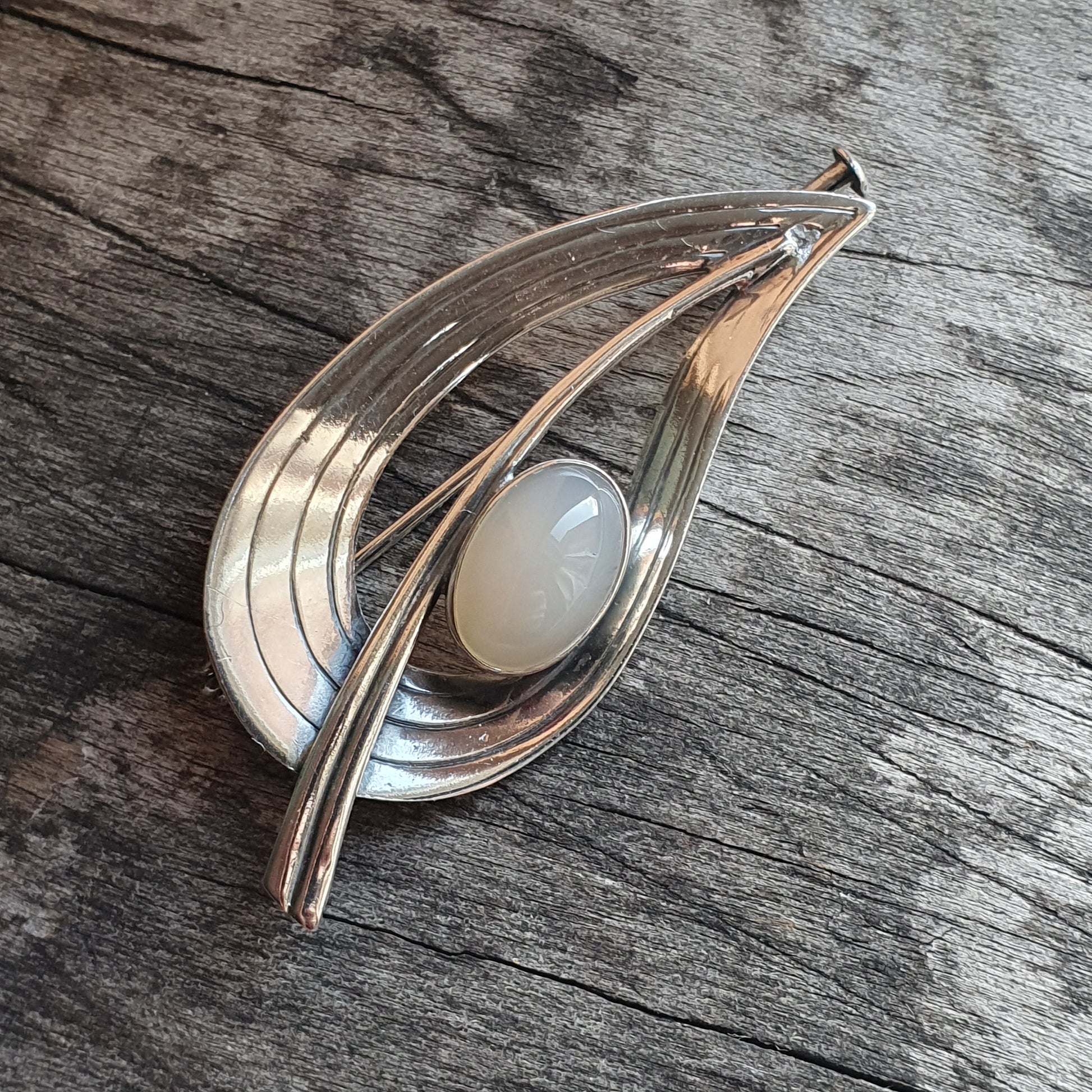 Teardrop-shaped silver brooch with a white gemstone in the center.