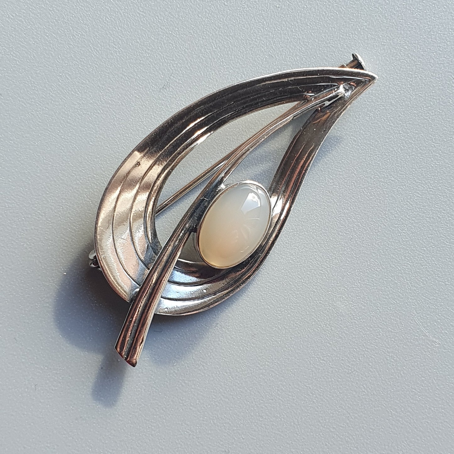 Teardrop-shaped silver brooch with a central opal or moonstone cabochon.