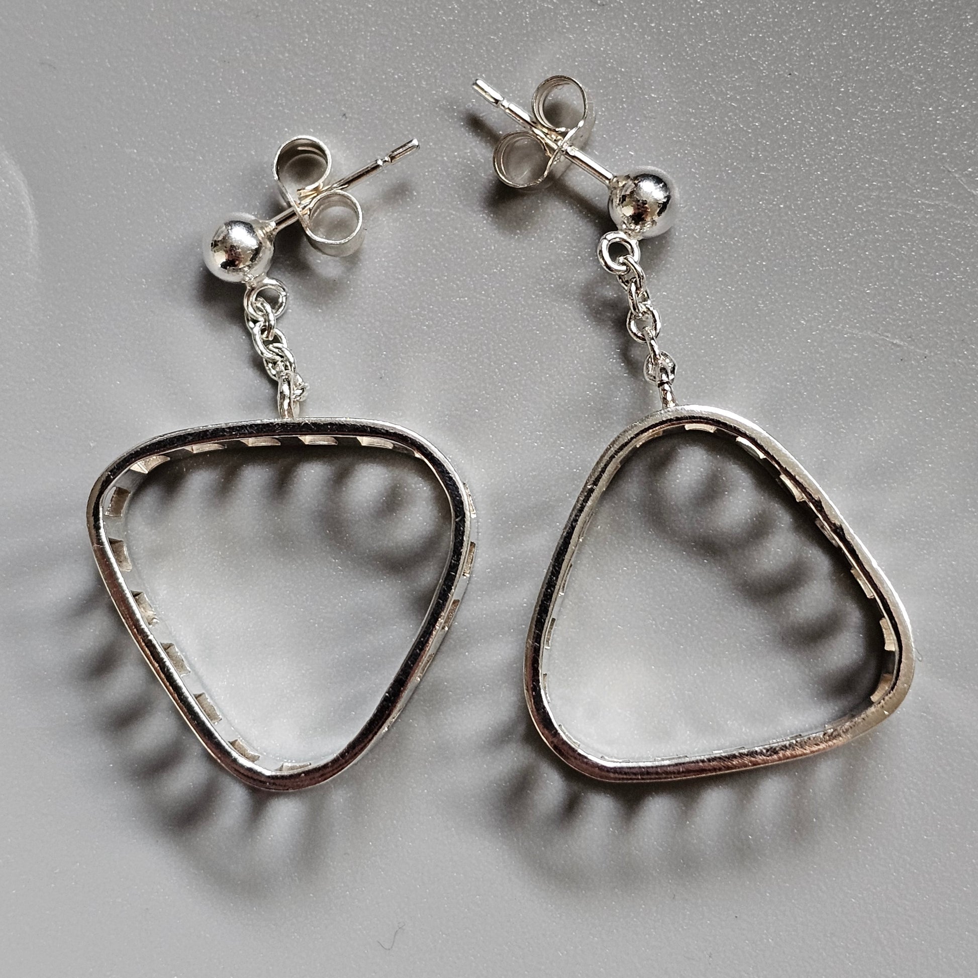 Pair of silver triangular-shaped dangle earrings with stud posts.