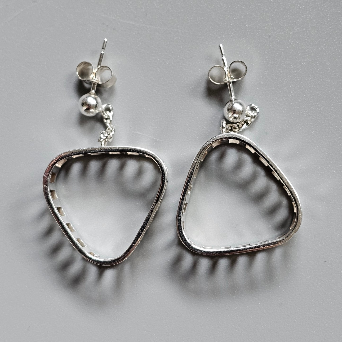 Pair of silver triangular-shaped dangle earrings with stud posts.