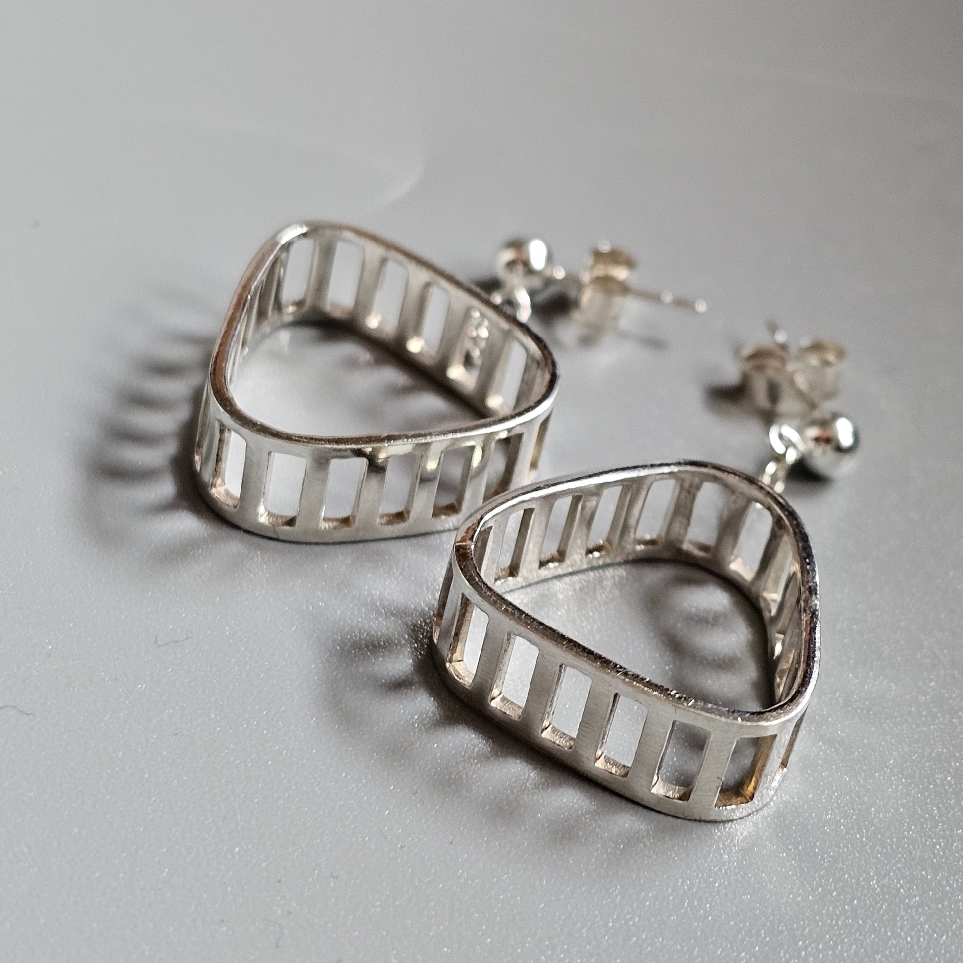 Pair of triangular silver earrings with ladder-like cutout designs.