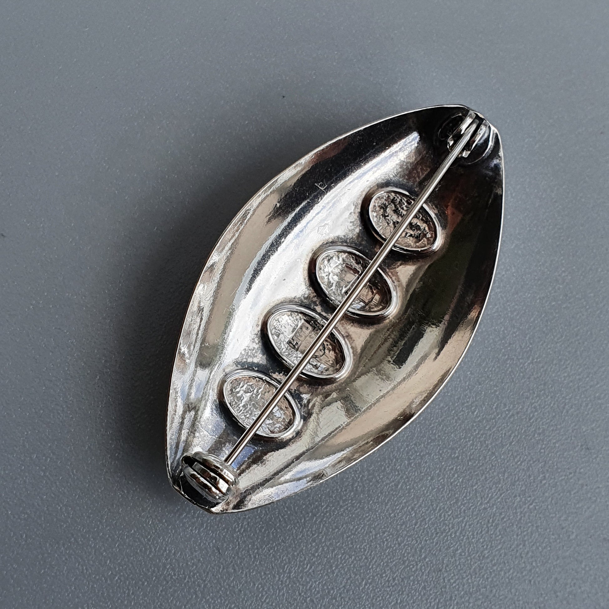 Silver-colored metal pendant or charm shaped like a football with decorative spiral pattern.