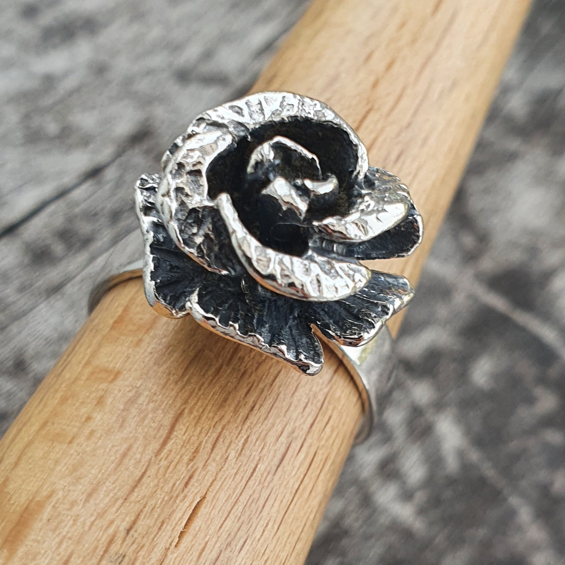 Silver rose-shaped ring with darkened accents on a wooden surface.