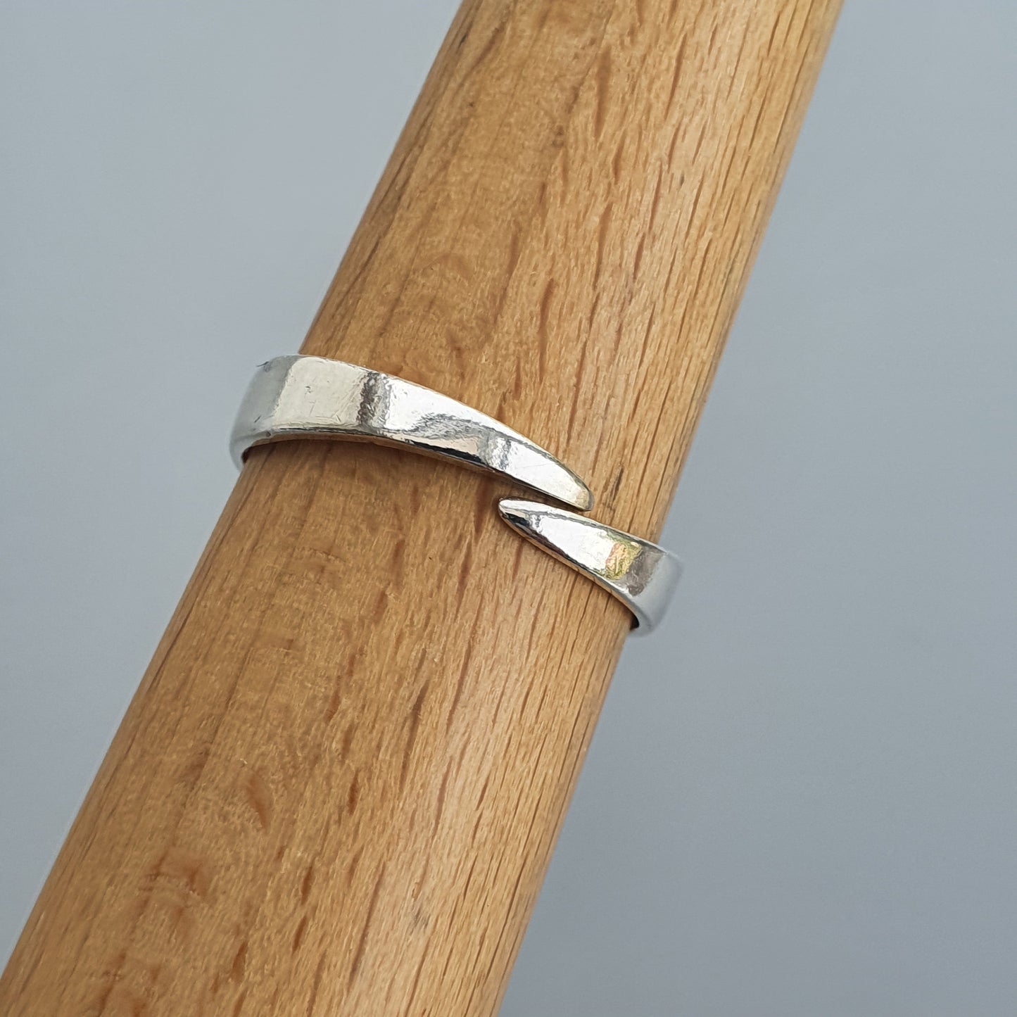 Silver ring with a twisted or overlapping design wrapped around a wooden surface.